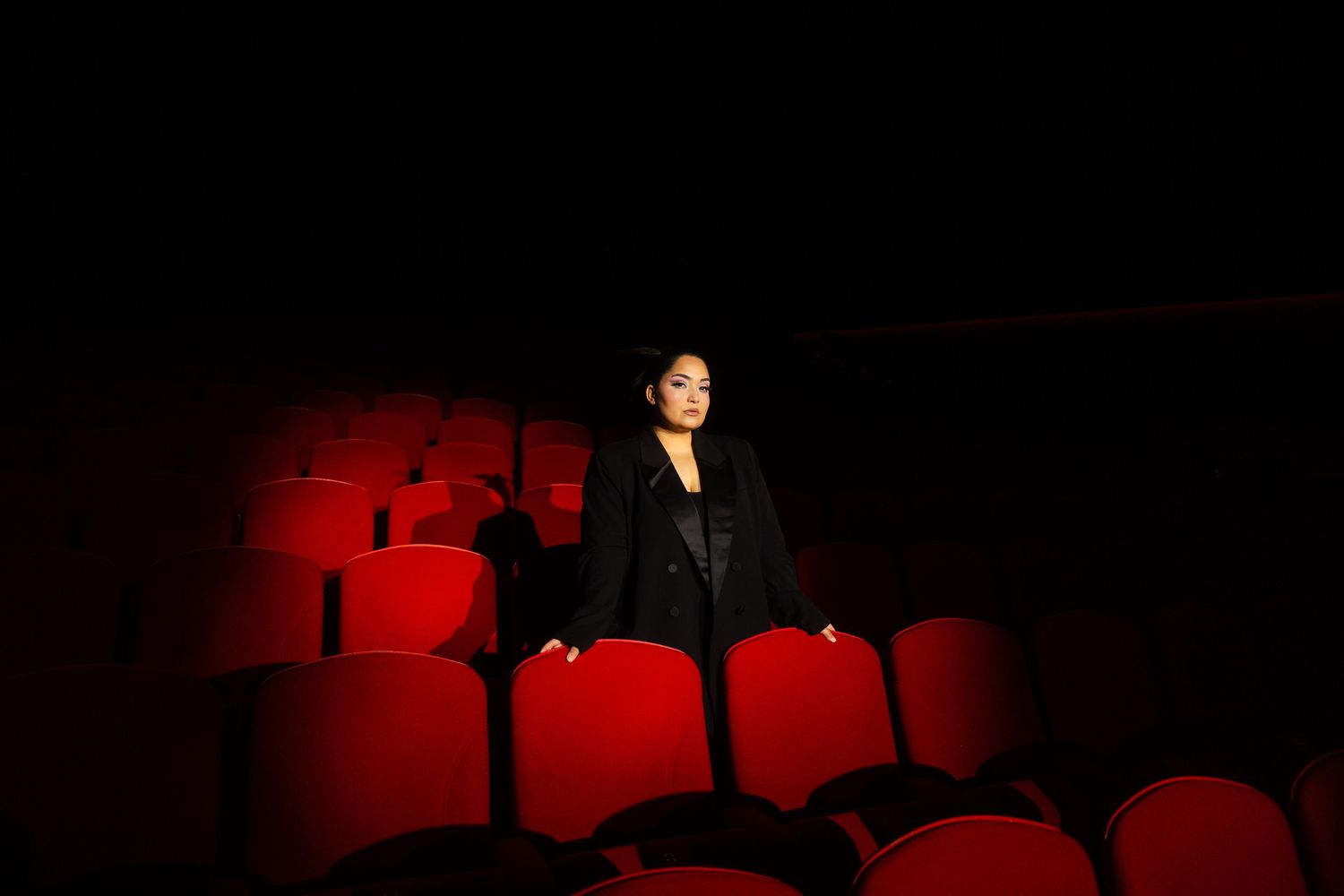 Bahar Kizil seated alone in empty theater with dramatic red lighting on vintage cinema seats, atmospheric cinema ambiance.