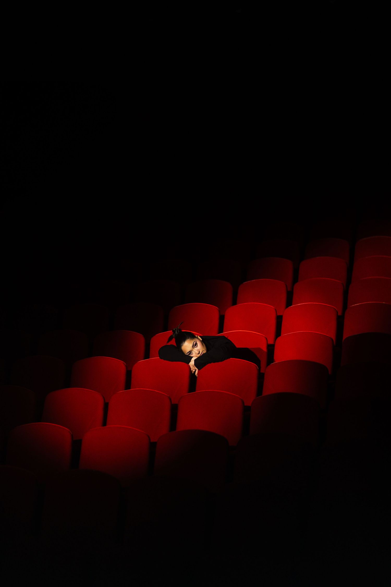 Bahar Kizil seated alone in empty theater with dramatic red lighting on vintage cinema seats.