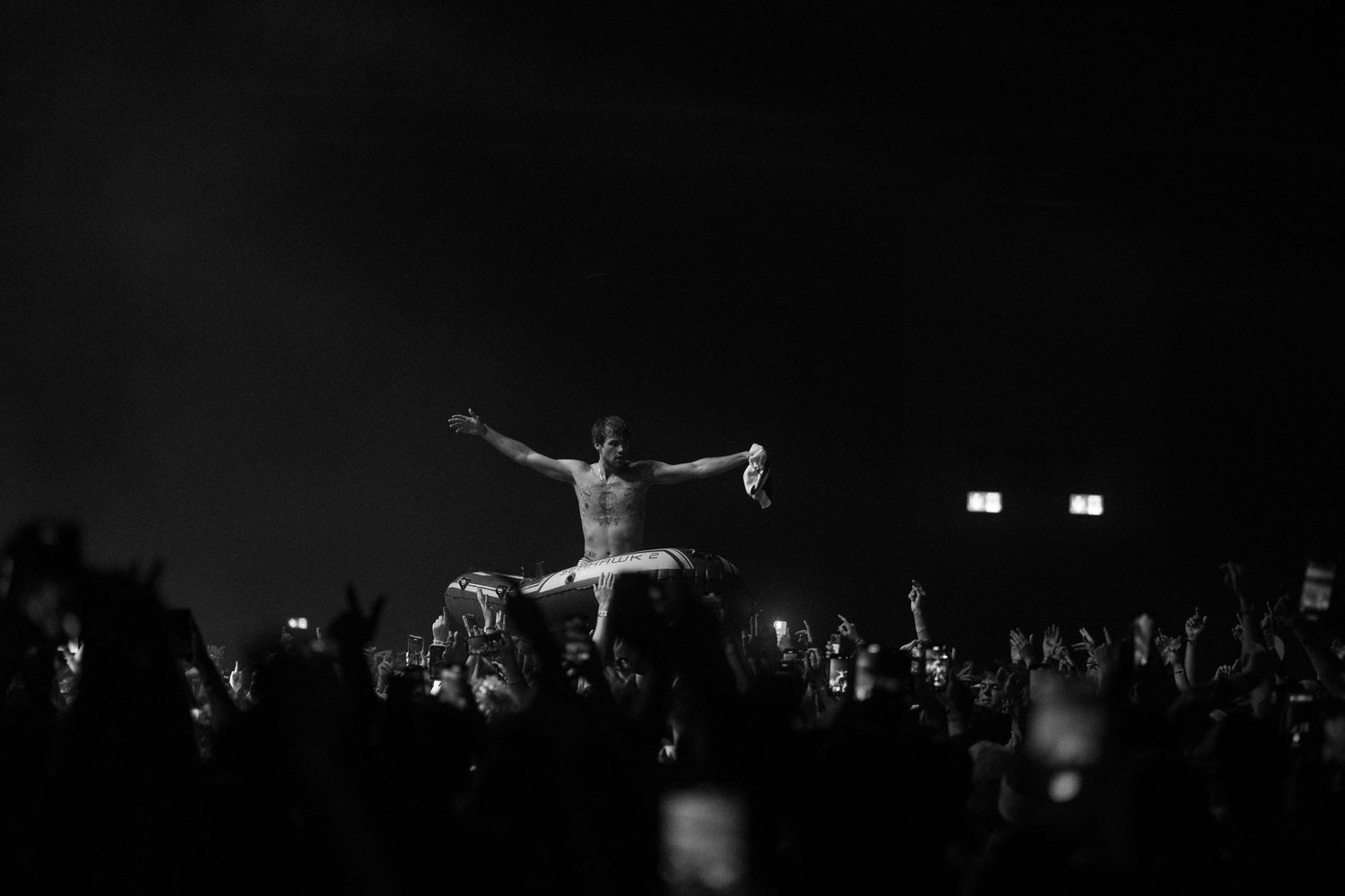 Silhouette of performer crowd surfing at night concert with audience holding phones.