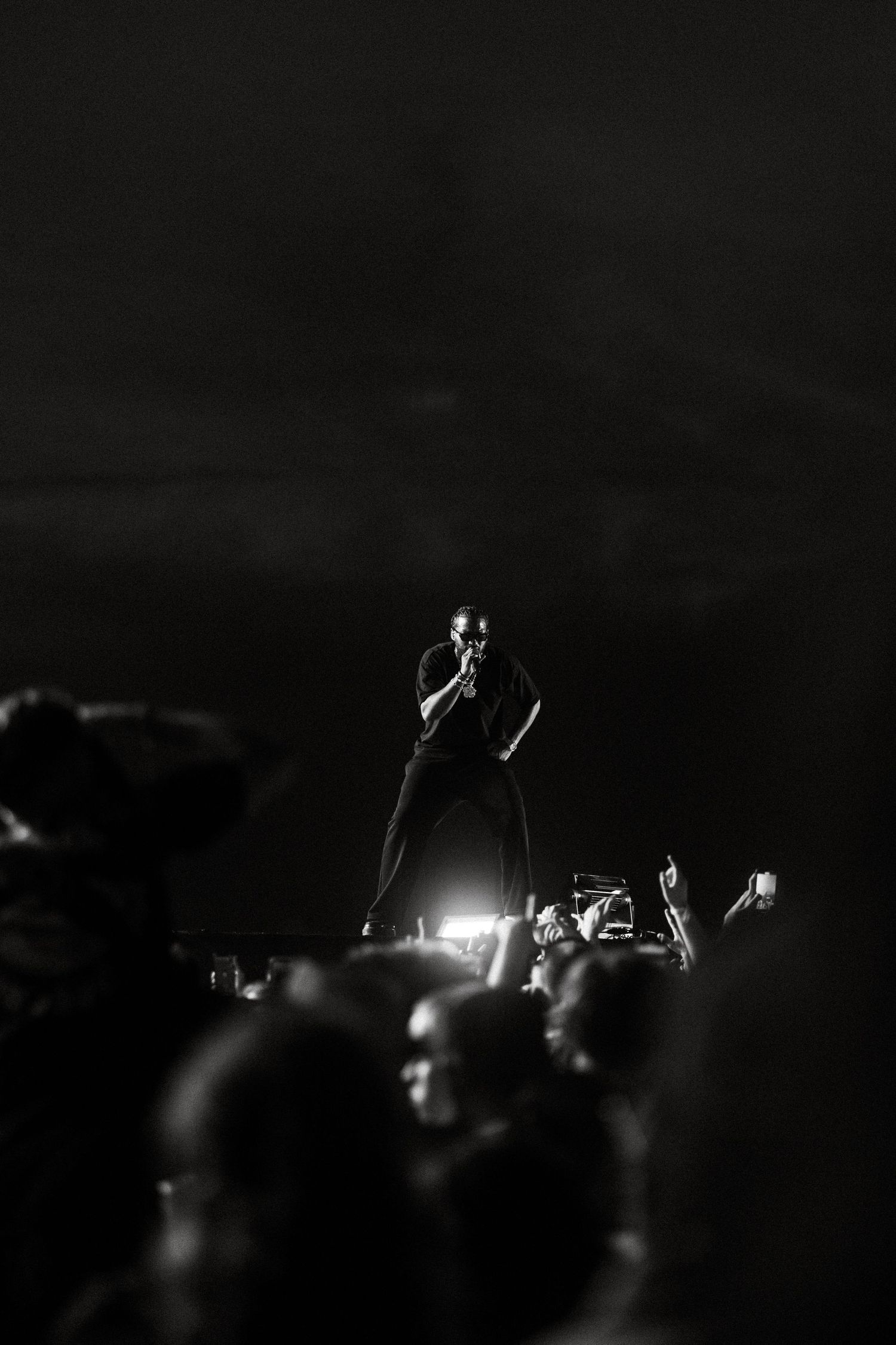 Dark concert crowd silhouettes illuminated by stage lights during a nighttime performance.