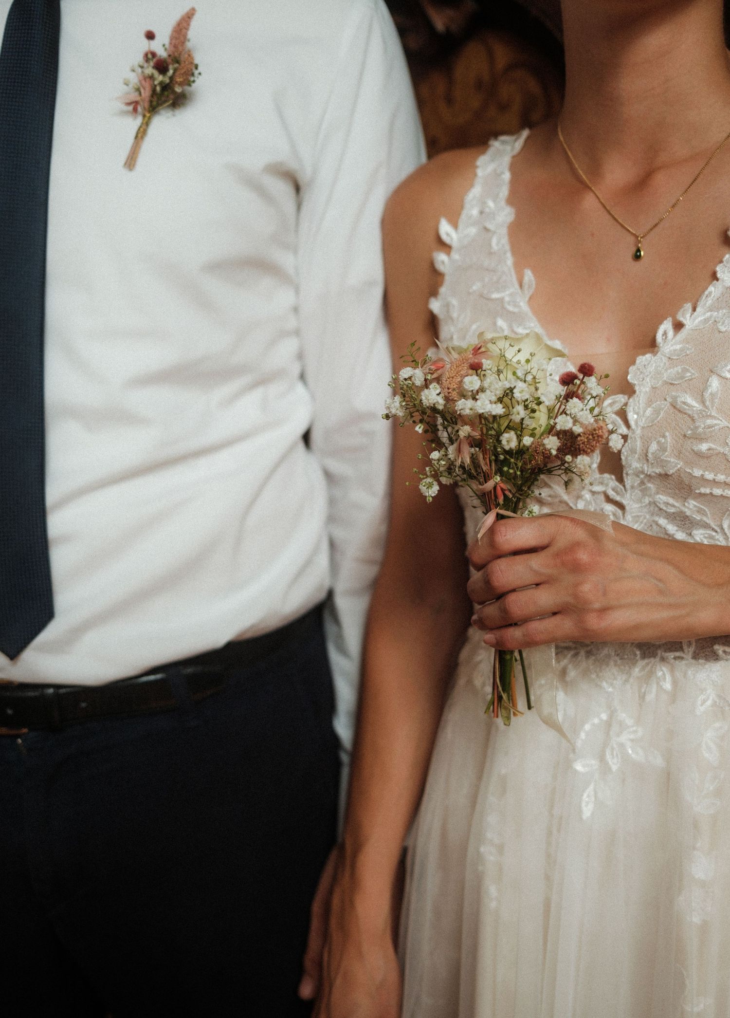 Close-up detail of wedding attire showing a boutonniere and bridal bouquet of baby's breath flowers.