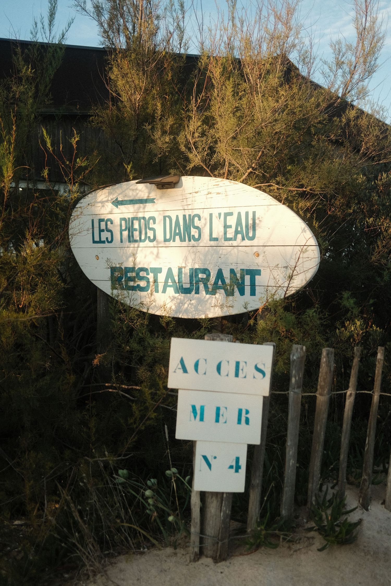 Weathered beach signs for restaurant 'Les Pieds dans l'eau' on wooden posts.