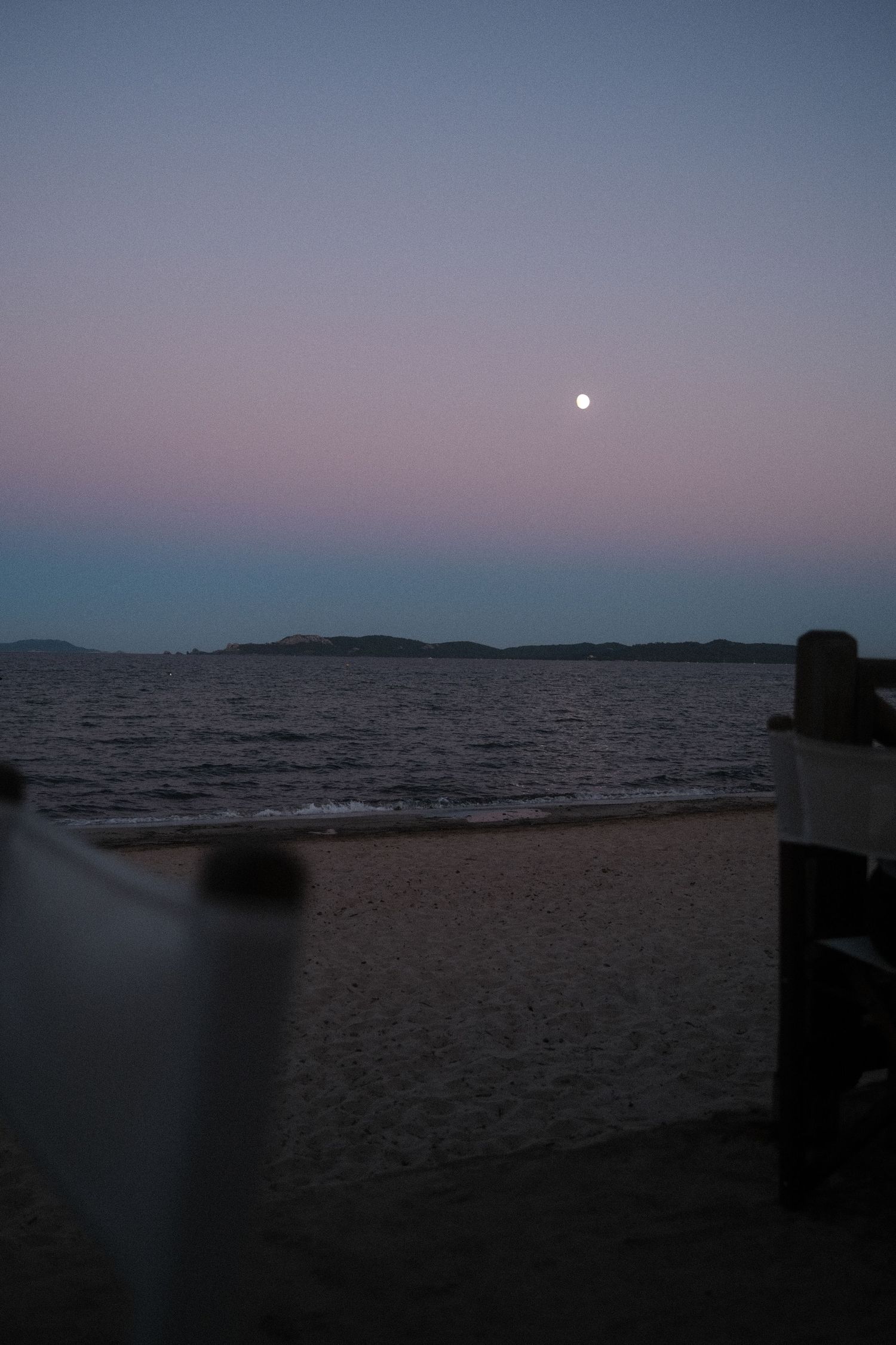 Peaceful twilight seascape with moon rising over calm waters and distant shoreline.