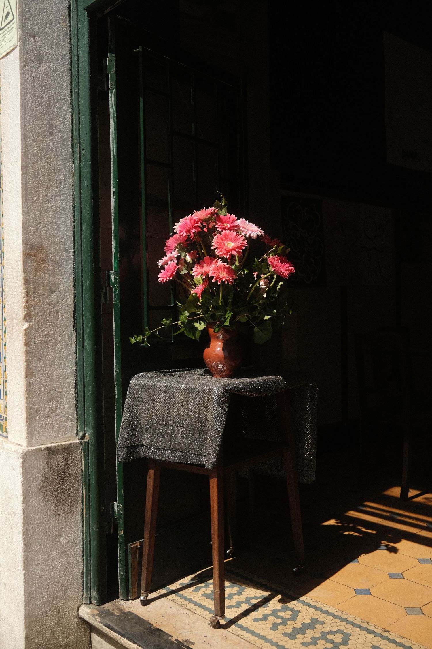 Pink flowers in vase on dark wooden stool with dramatic lighting.