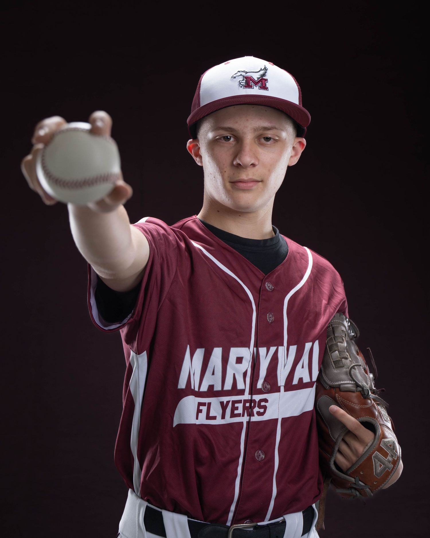 Maryvan Flyers baseball player in maroon uniform holding a ball toward the camera with a glove in hand.
