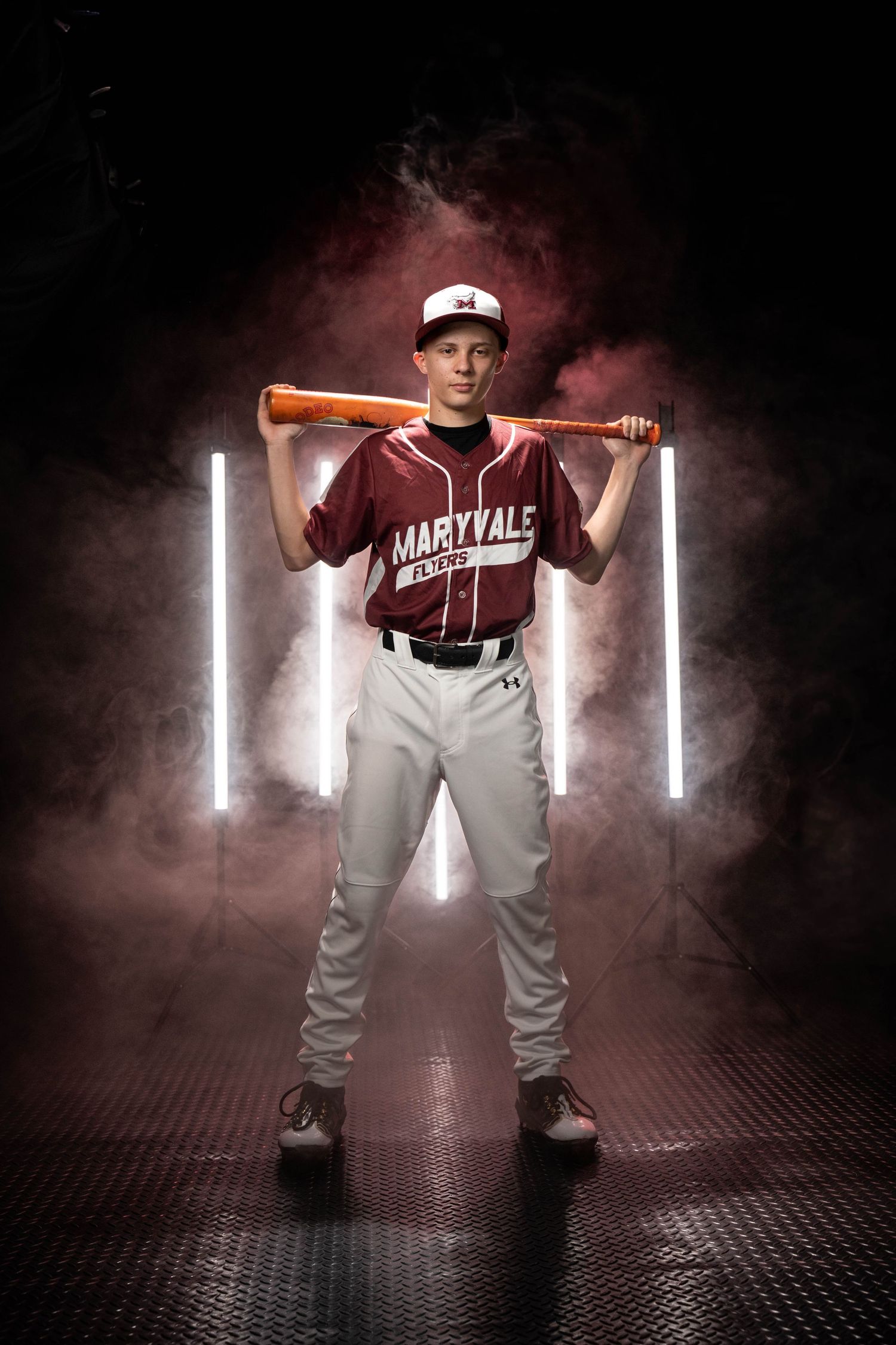 Young baseball player in Maryvale uniform holding bat behind shoulders posed dramatically with neon lights and smoke.