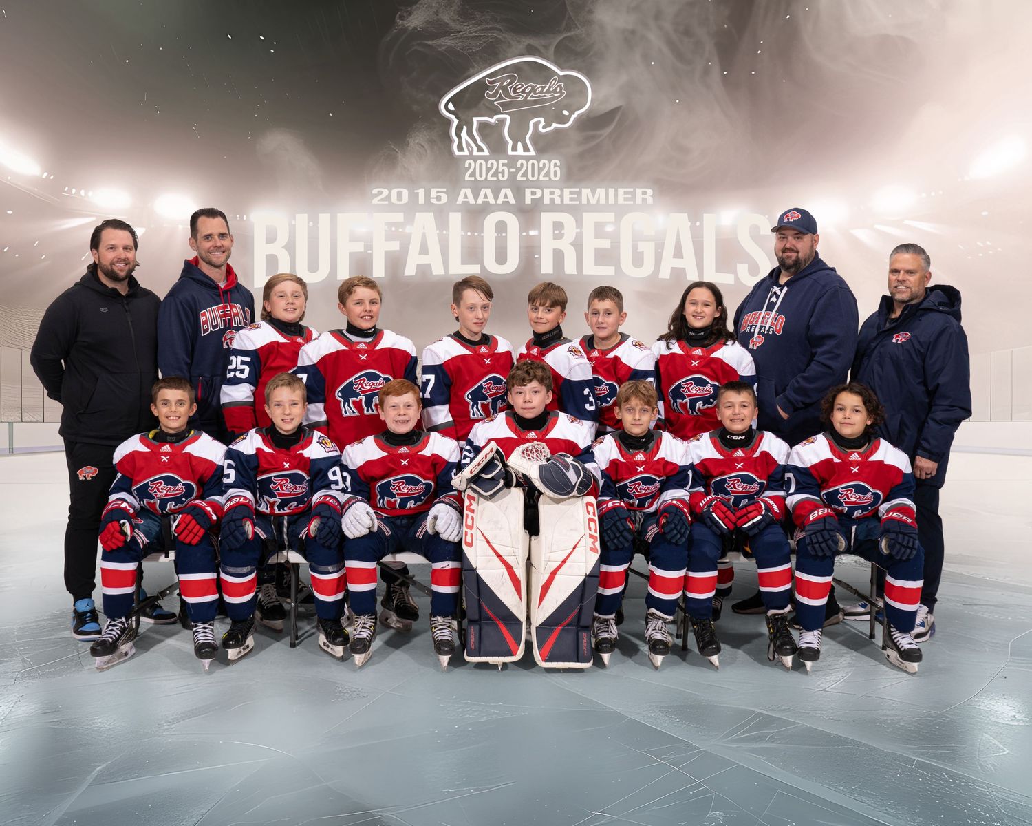 Youth hockey team poses for group photo in red and blue jerseys on ice rink with coaches and staff members.