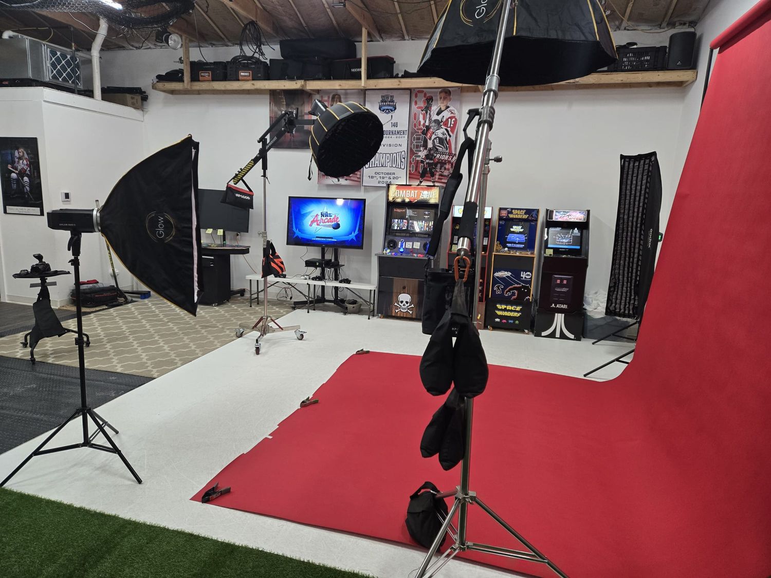 Professional photography studio setup with red backdrop, lighting equipment, monitors and video gear.