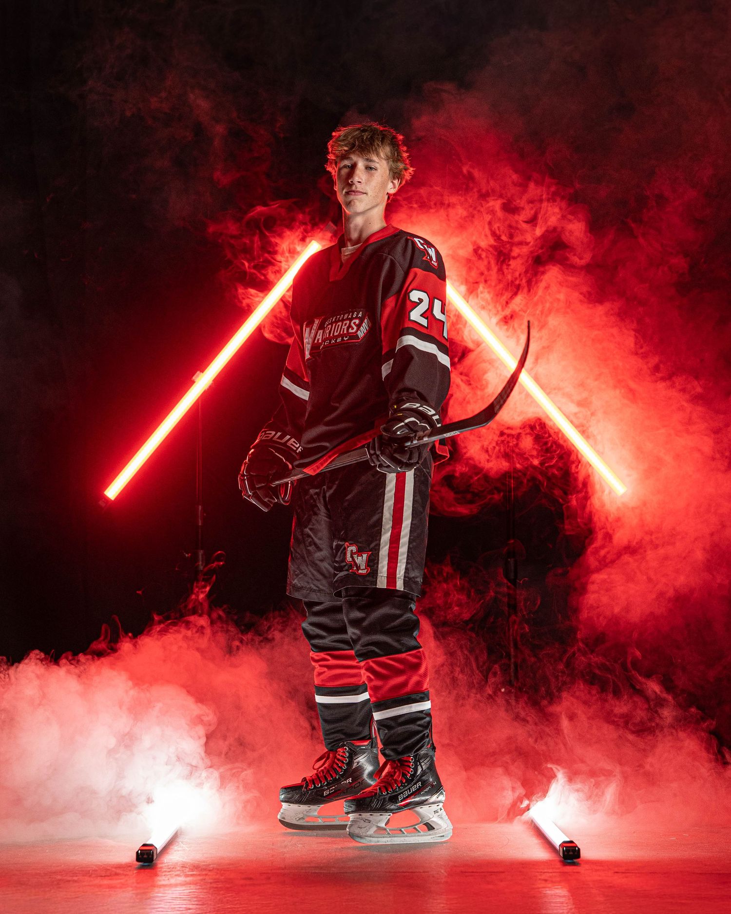 Hockey player poses dramatically in dark uniform with red lighting and smoke effects creating an atmospheric sports portrait.