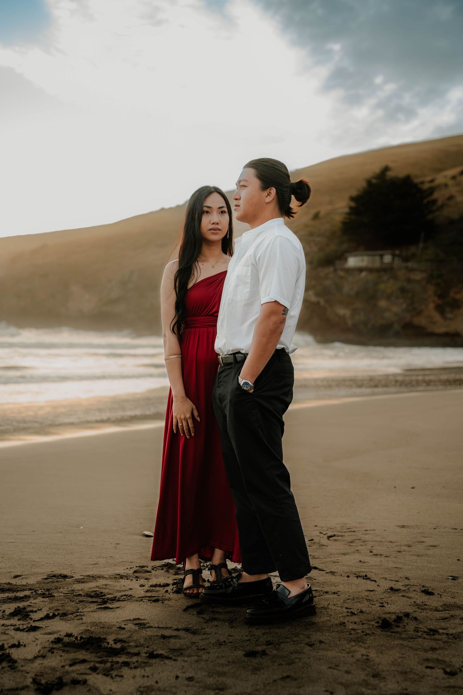 A couple shares an intimate moment together on a sandy beach at sunset with dramatic cloudy skies in the background.