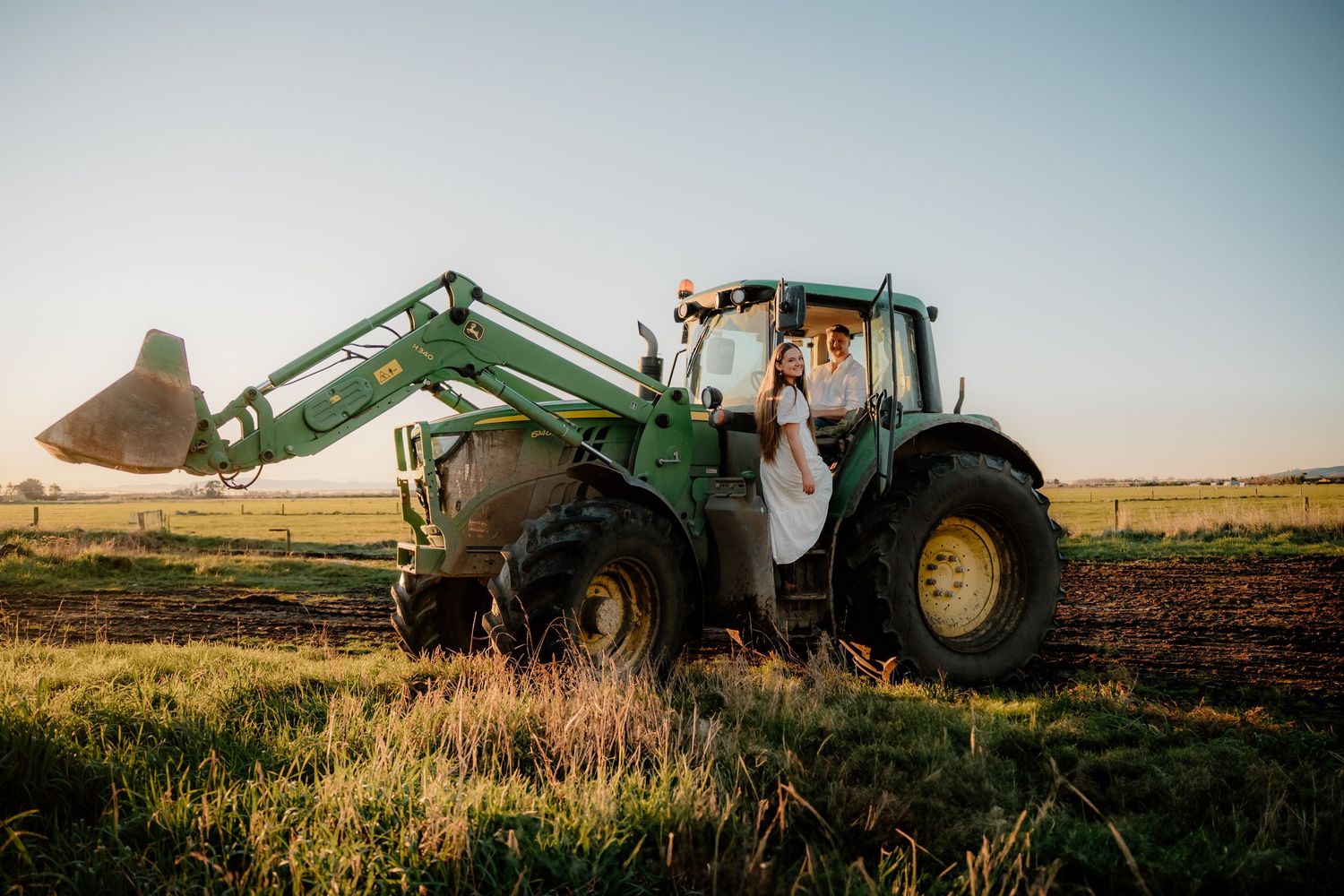 John Deere tractor working in a farm field at sunset kicking up dust during golden hour.