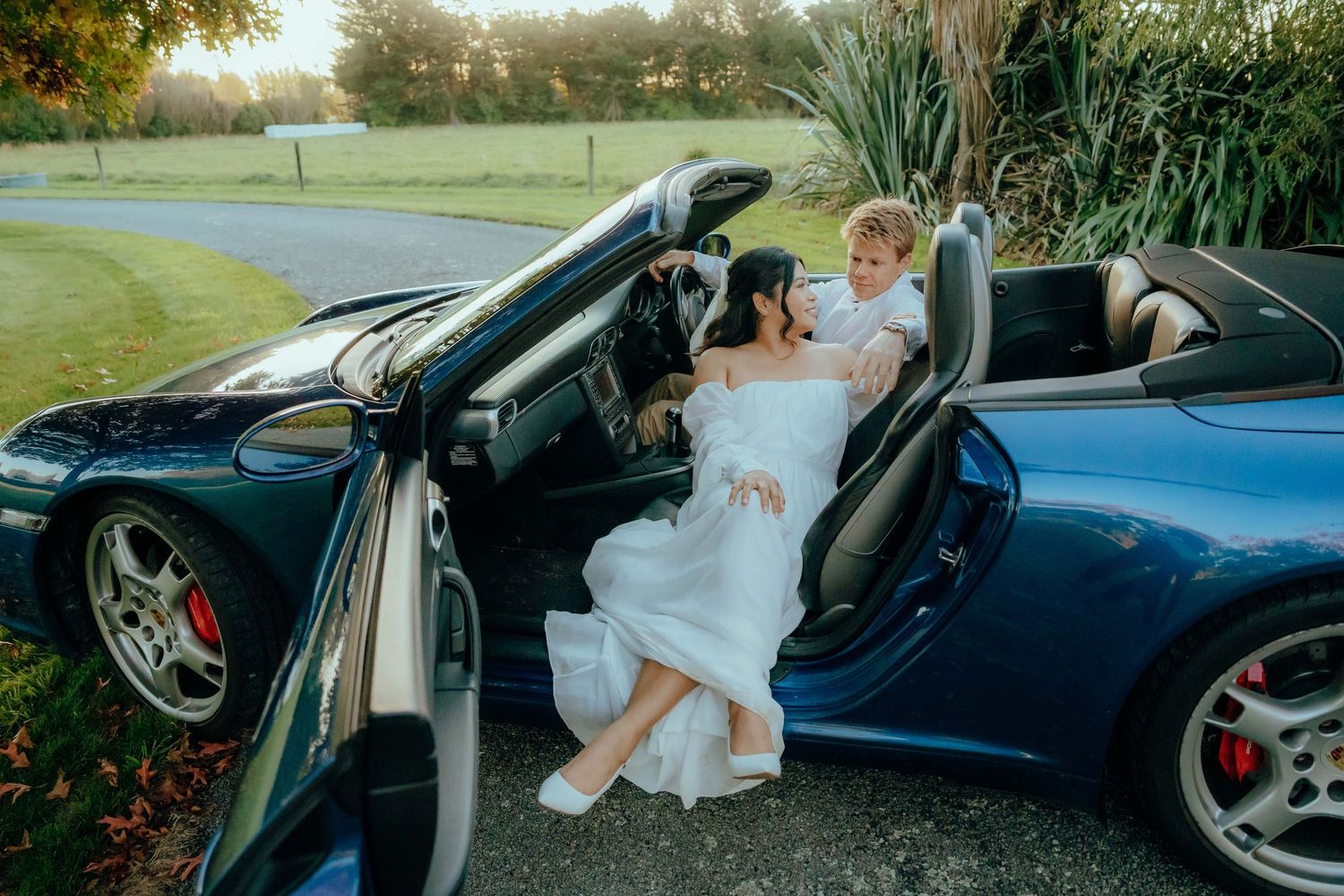 A person in a white dress sits gracefully in a luxury convertible car on a sunny day.