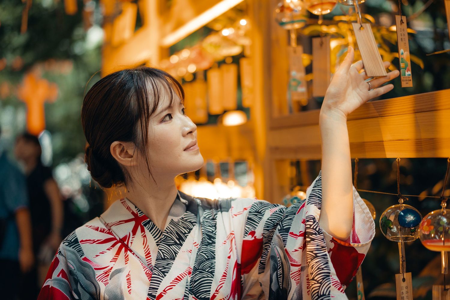 Asian woman in red traditional dress decorates lanterns at night in an atmospheric setting.