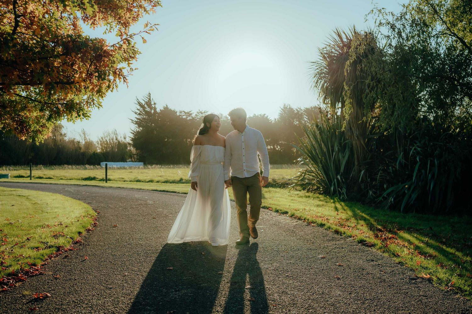 A couple walks down a sunlit path surrounded by autumn trees and golden light during a romantic evening stroll.