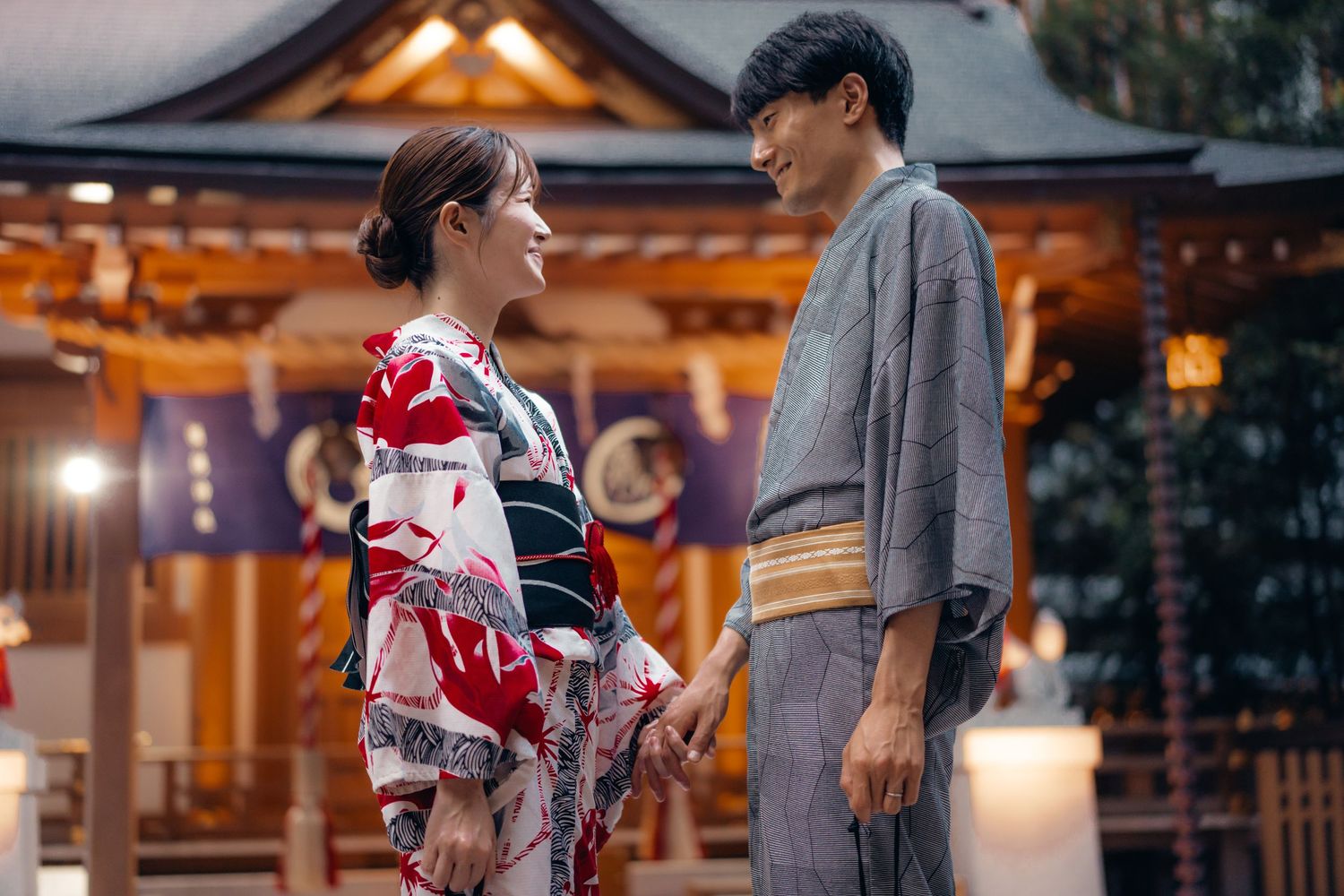 Traditional Japanese wedding ceremony with couple in kimono and hakama standing at a temple shrine at sunset.
