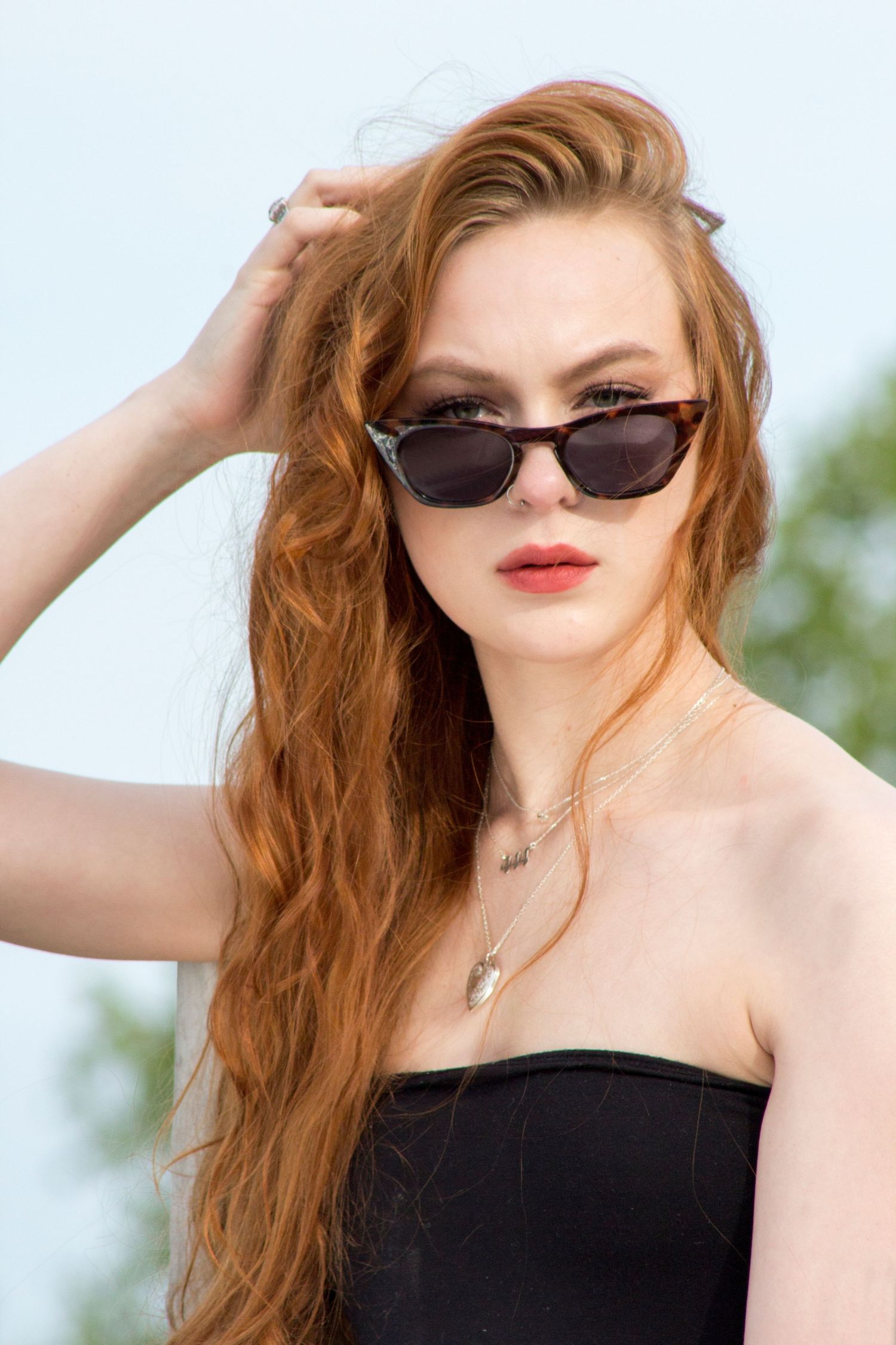 An artistic image of a woman looking over her sunglasses at the camera while fixing her hair.