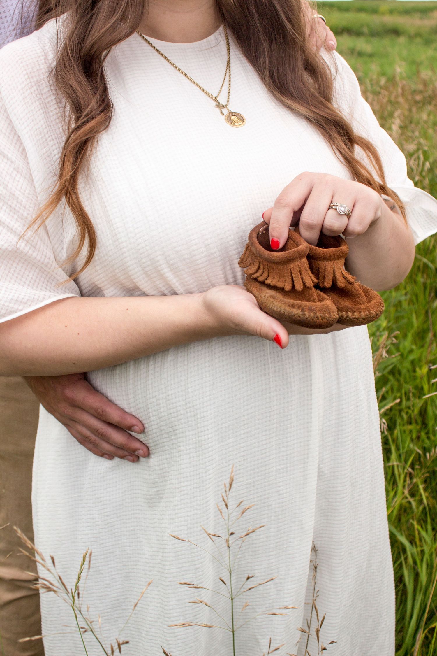 Maternity photo with a woman holding a pair of baby shoes.