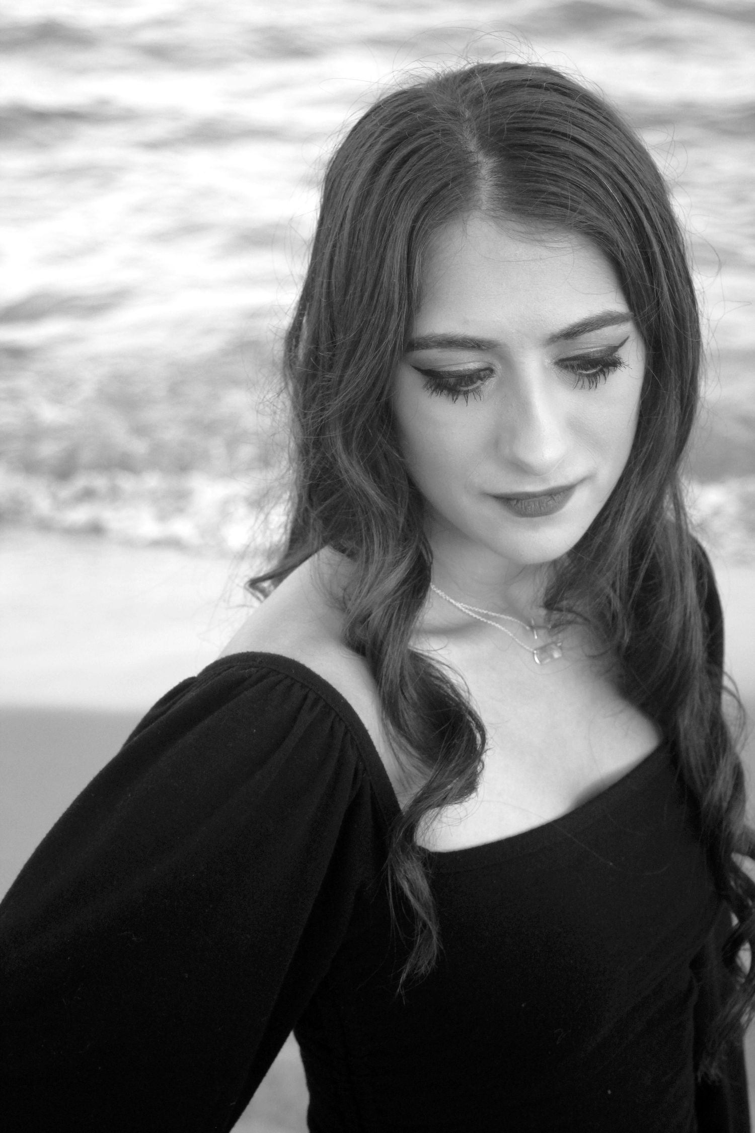 An artistic image of a women in black and white with the beach behind her.