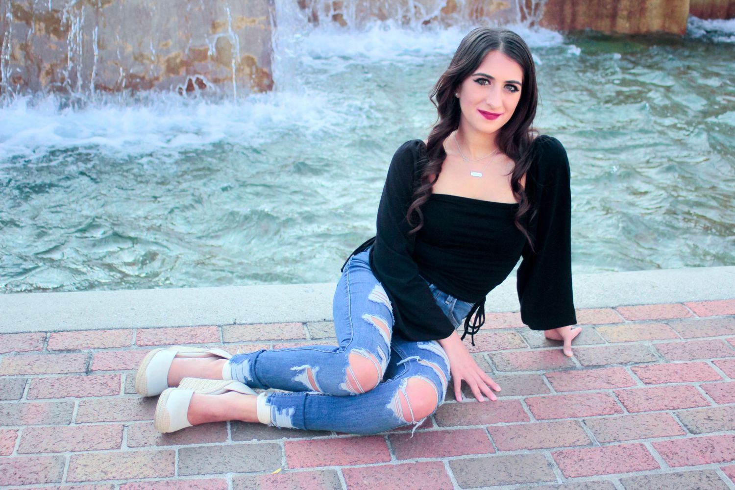 An image of a woman posing on her side in front of a water fountain.