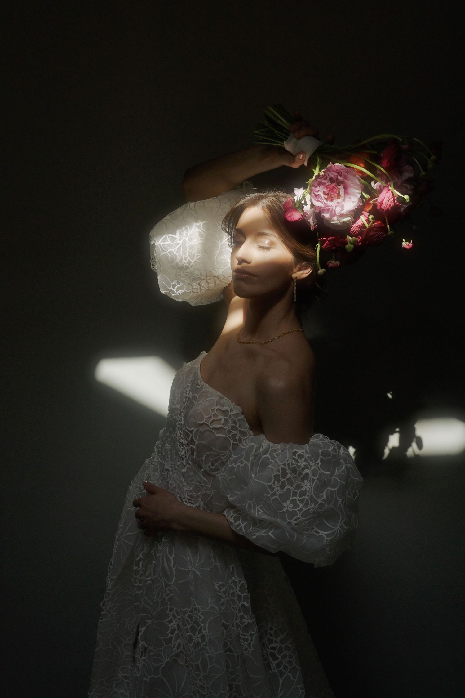 Artistic portrait of someone in white lace with pink flowers and dramatic lighting against dark background.