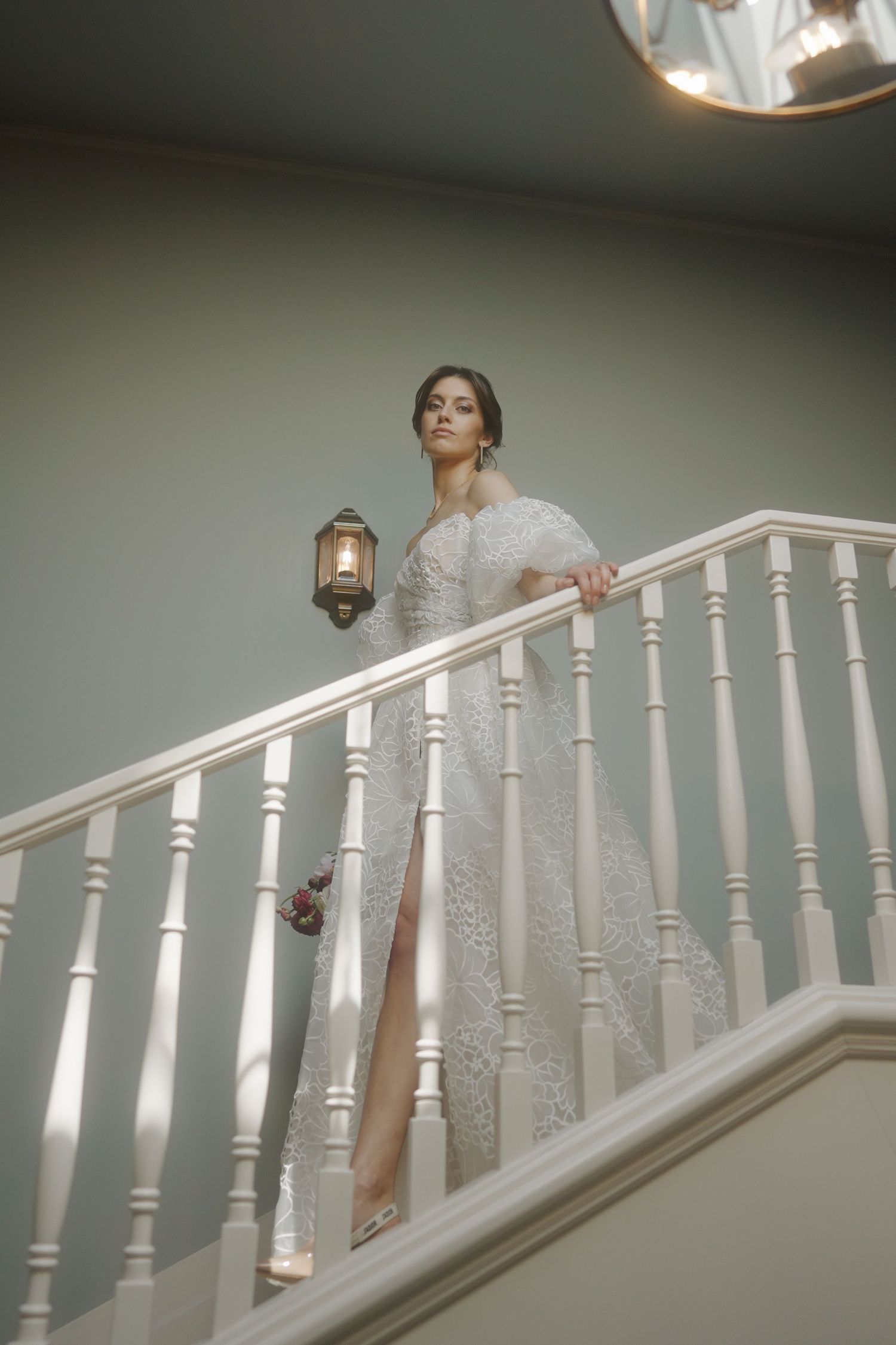 Elegant figure in a white lace gown standing on a staircase holding a vintage lantern.