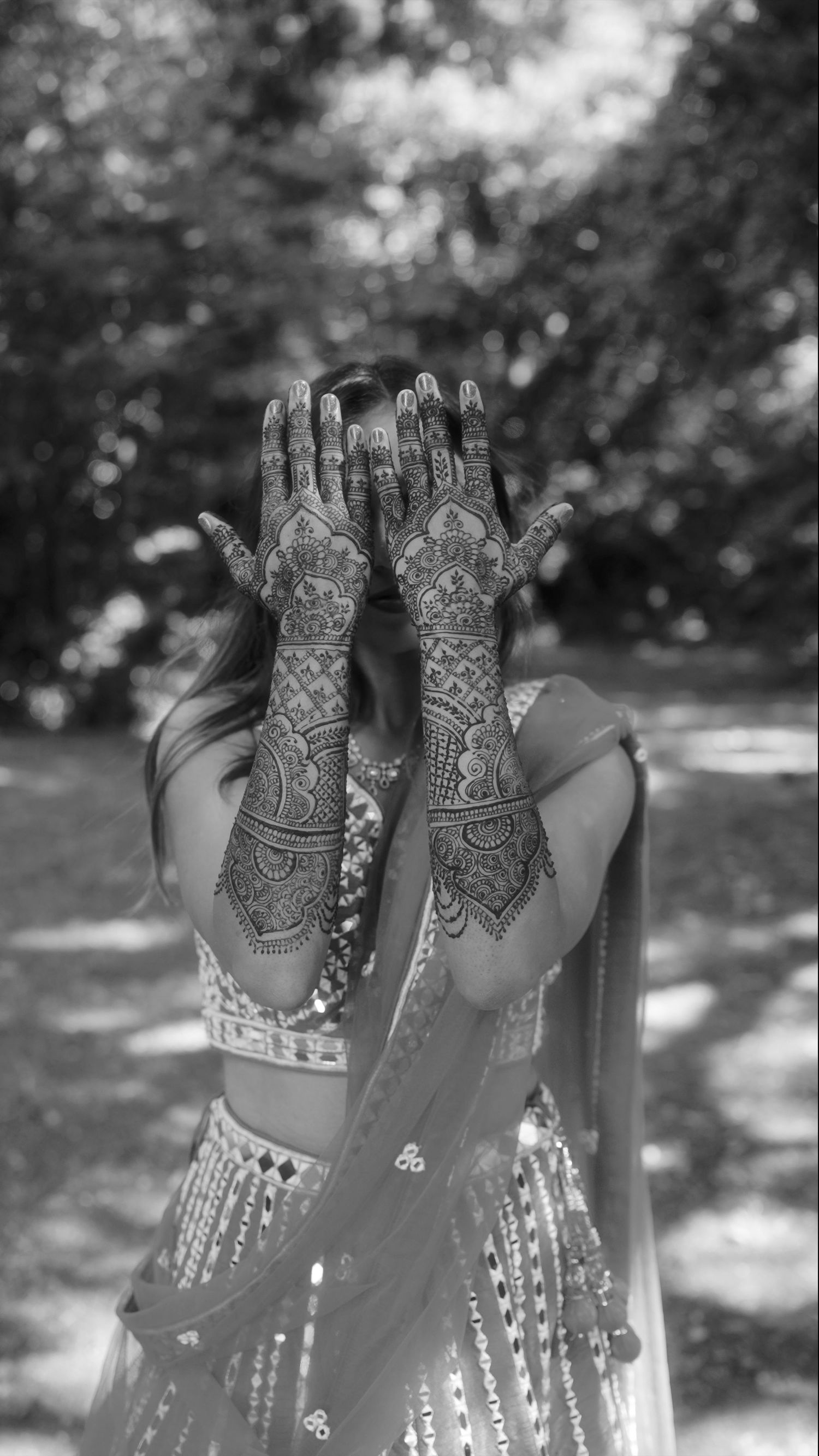 Detailed henna designs on raised hands against a blurred natural background.