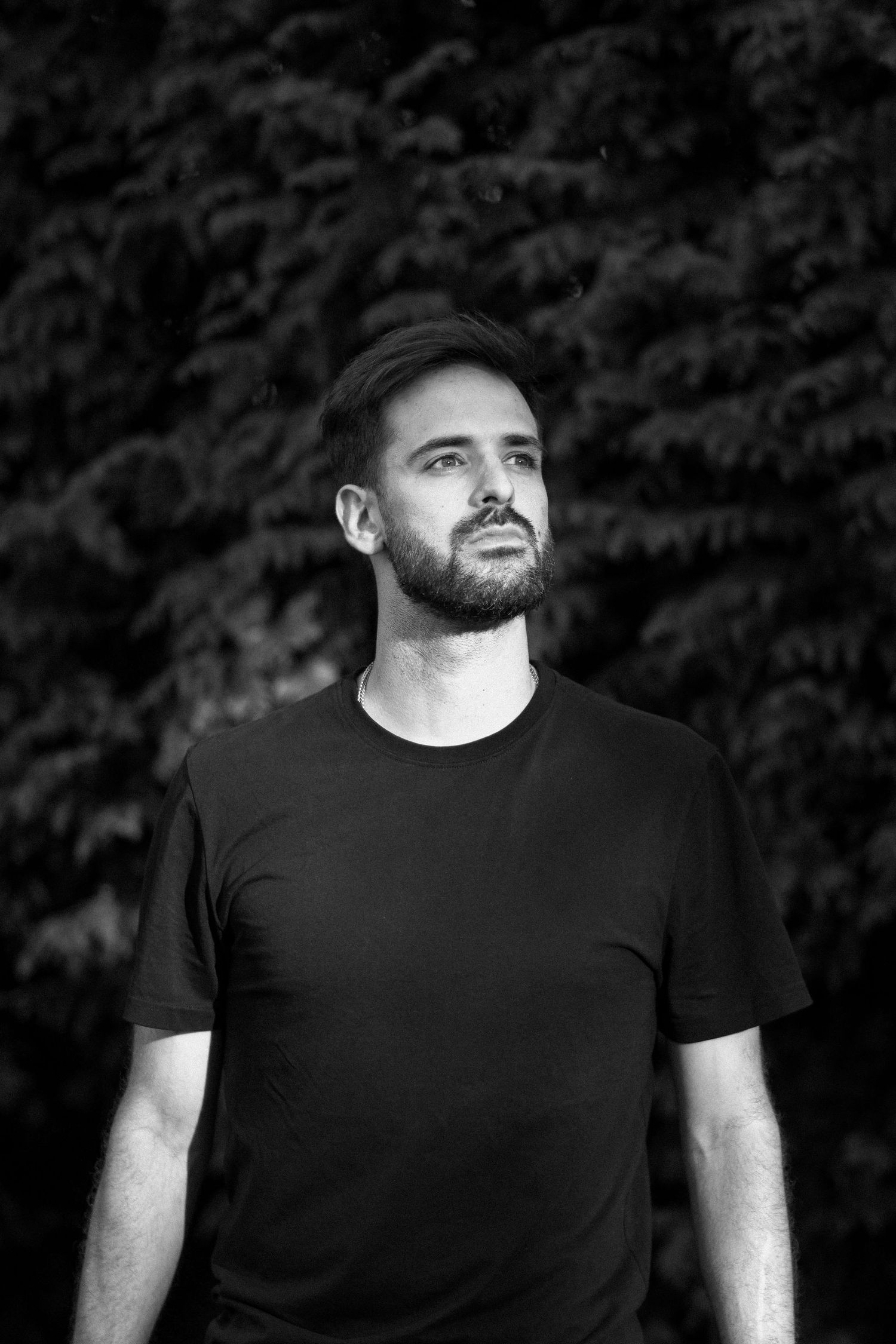 Black and white portrait of a bearded man in a dark t-shirt against a blurred nature background.