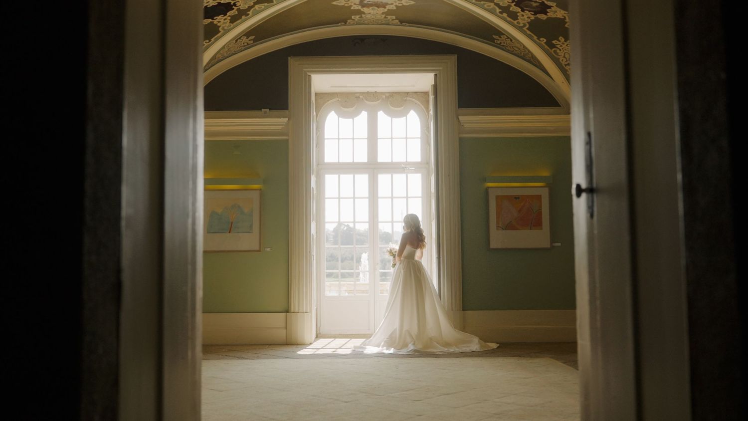 Vintage-style photo of a bride silhouetted against bright windows in a grand room.