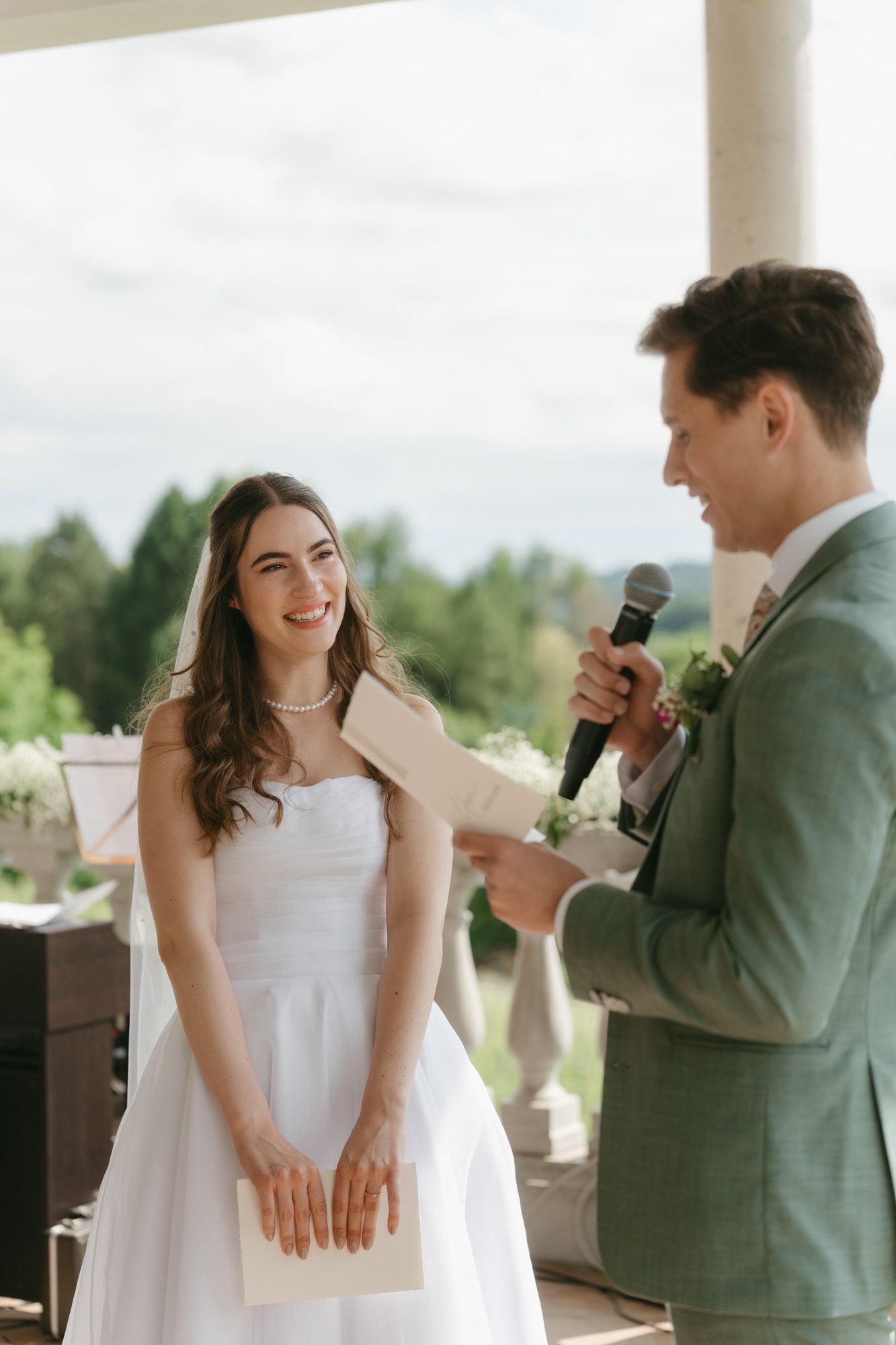 A wedding ceremony moment with two people sharing laughter during a speech outdoors.