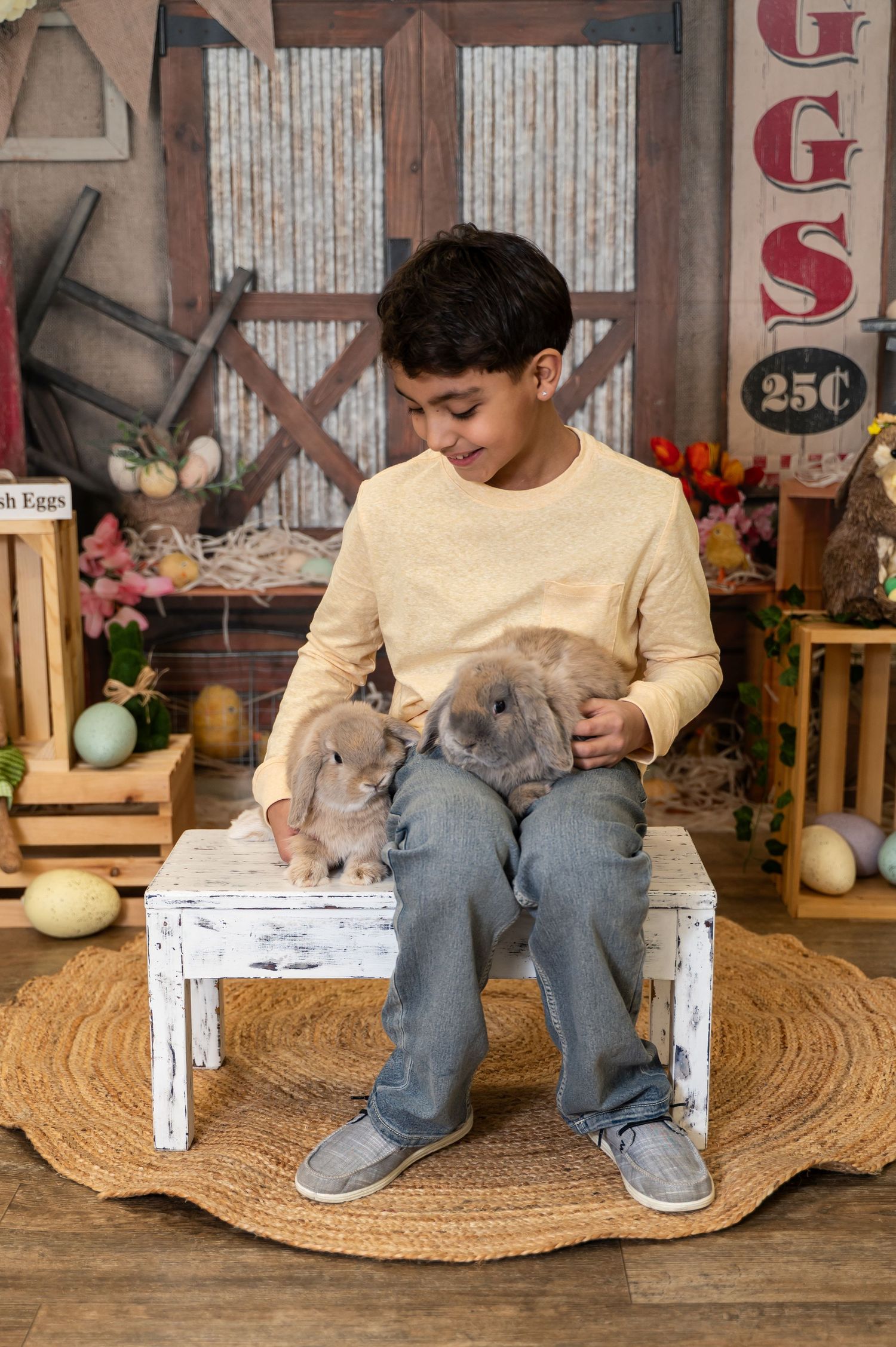 A person in a cream sweater and jeans sits on a rustic wooden bench with a fluffy gray bunny rabbit in their lap.