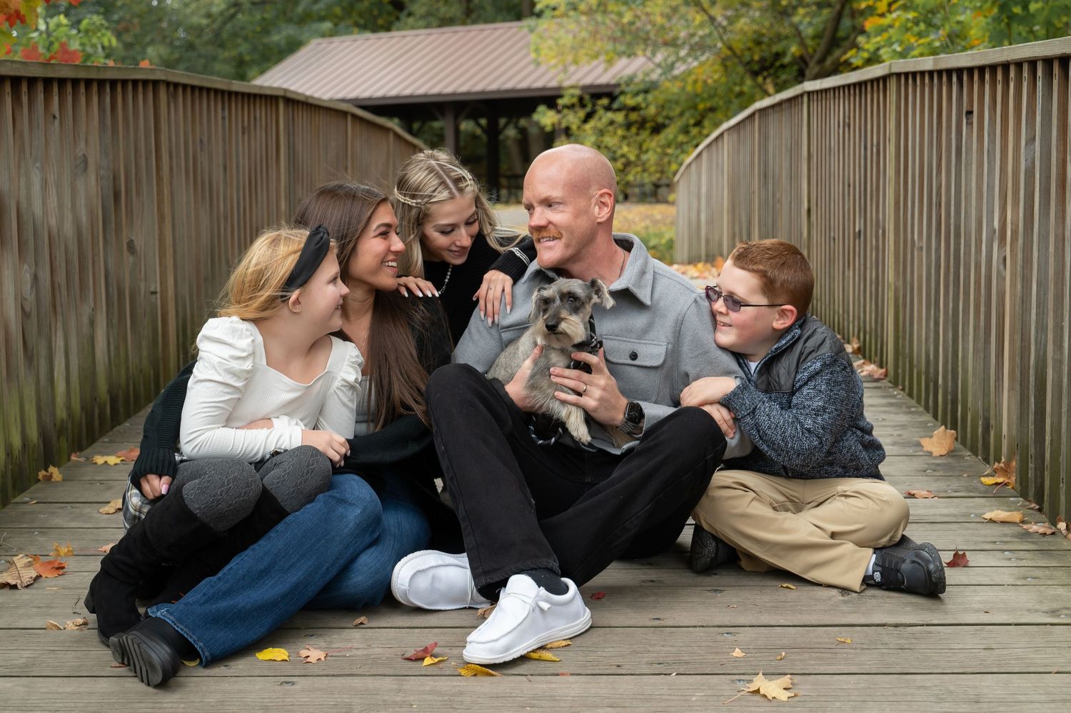 Candid lifestyle photo of group laughing together with puppy on rustic wooden bridge.