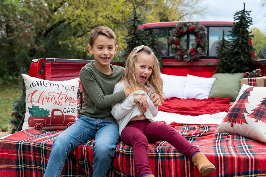 Two people sit on a red plaid blanket in a truck bed decorated for Christmas.