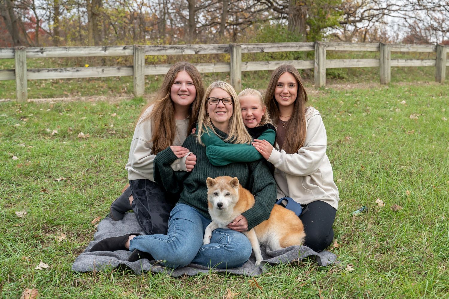 Four people sitting on grass with corgi dog during fall outdoor portrait session.
