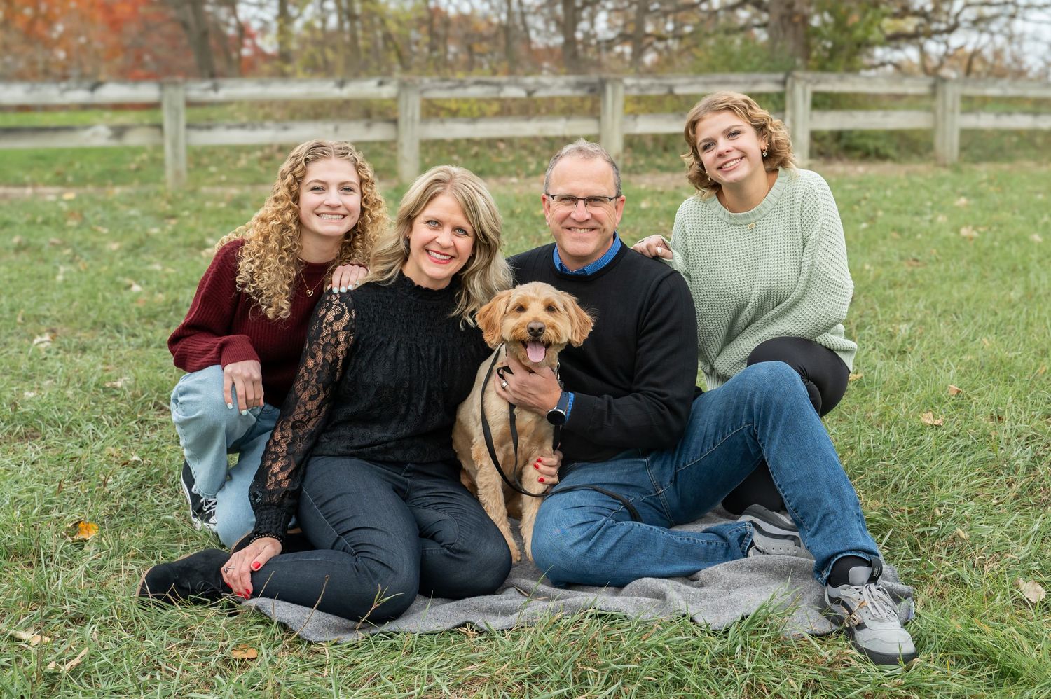 family and dogs sitting in front of a fence