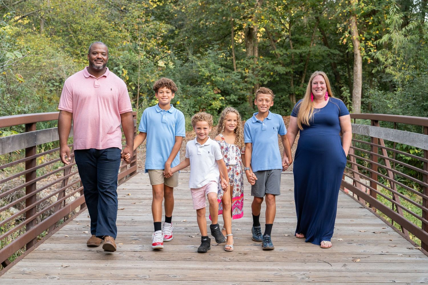 Family of six walking together and holding hands on a wooden bridge in a park setting during autumn.