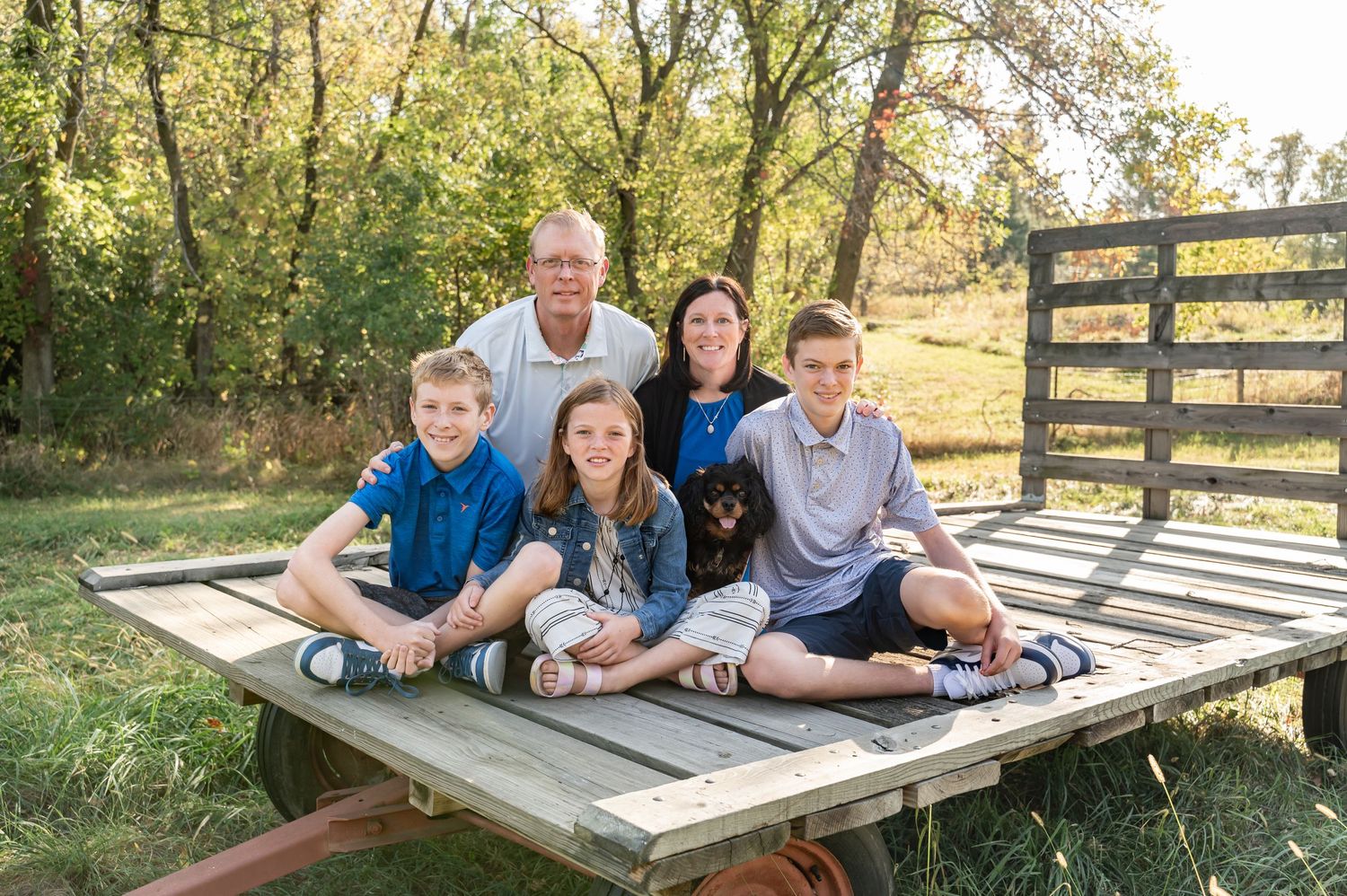 Family of five relaxing on wooden platform deck during outdoor photo session.