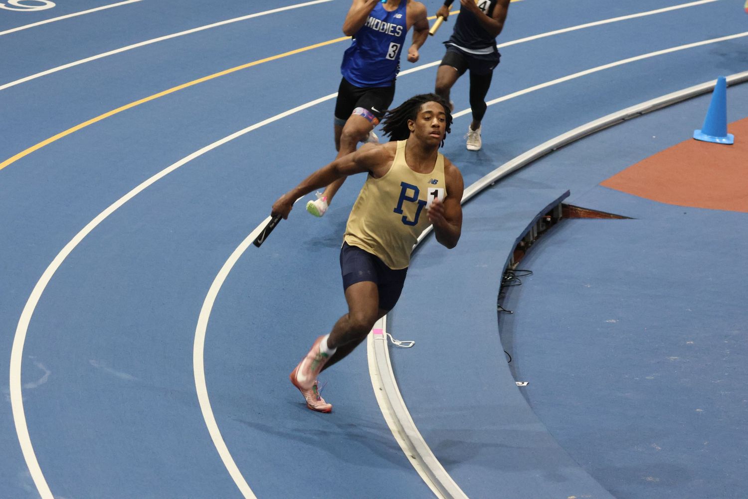 Female sprinter racing on an indoor blue track during a relay competition.