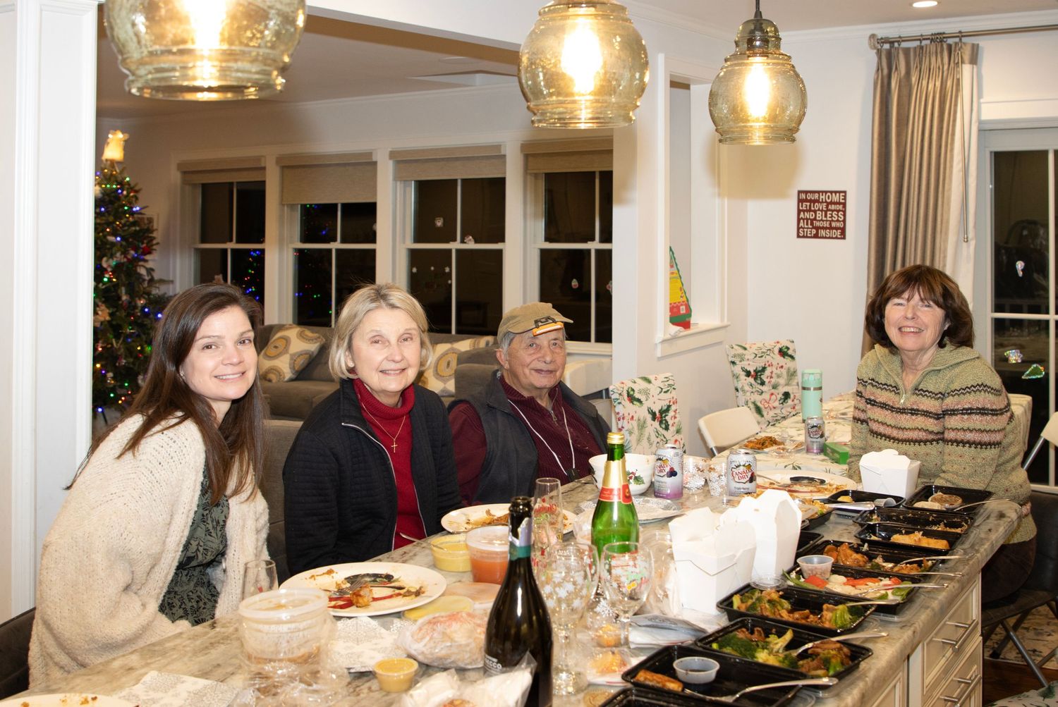 Four women smiling at a festive dinner table with food, wine, and elegant pendant lighting.