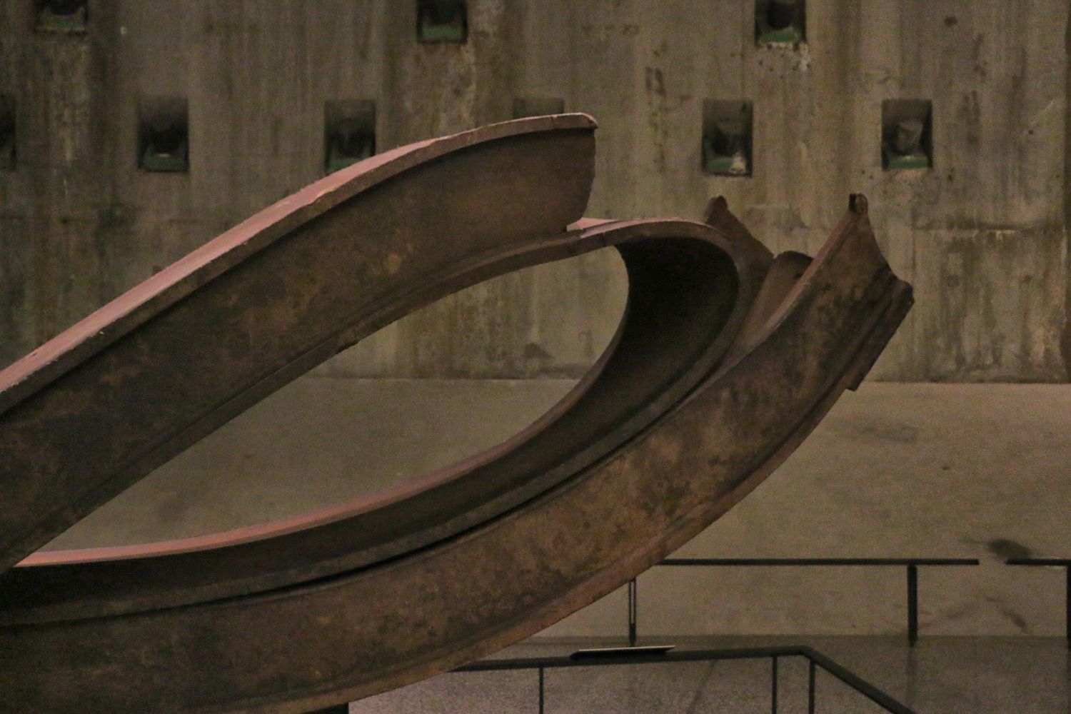 Twisted steel beam sculpture artifact from 9/11 memorial displayed against concrete wall.