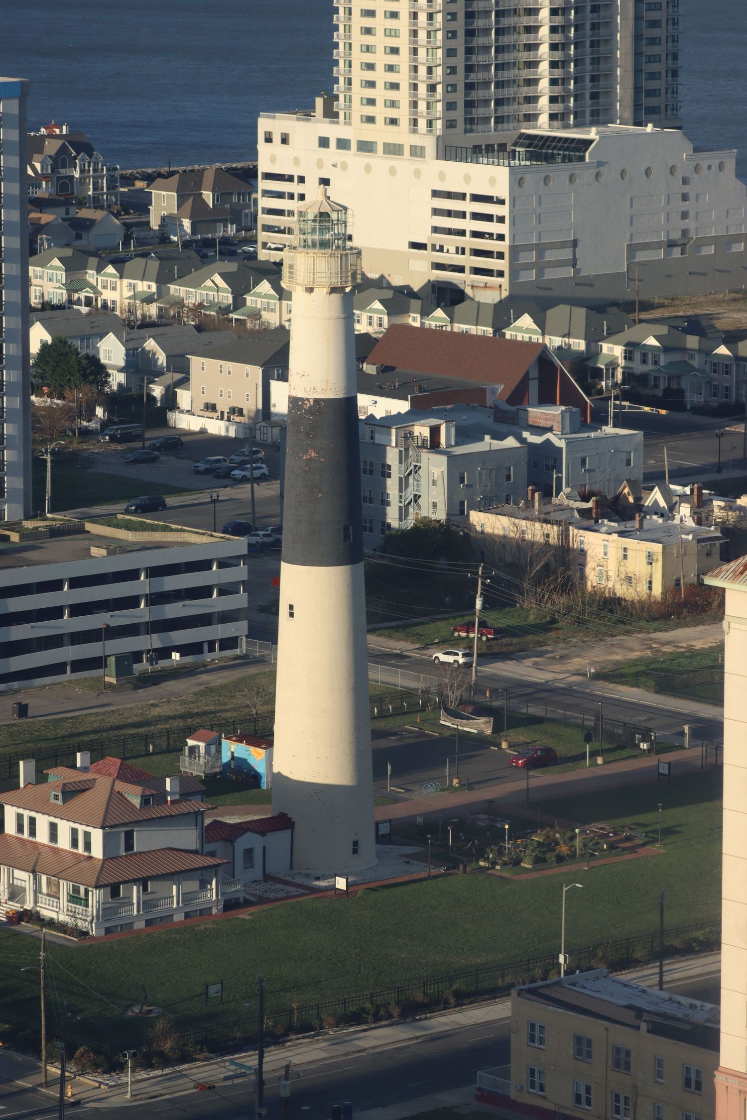 Aerial view of Absecon Lighthouse tower rising above Atlantic City neighborhoods with ocean visible in background.