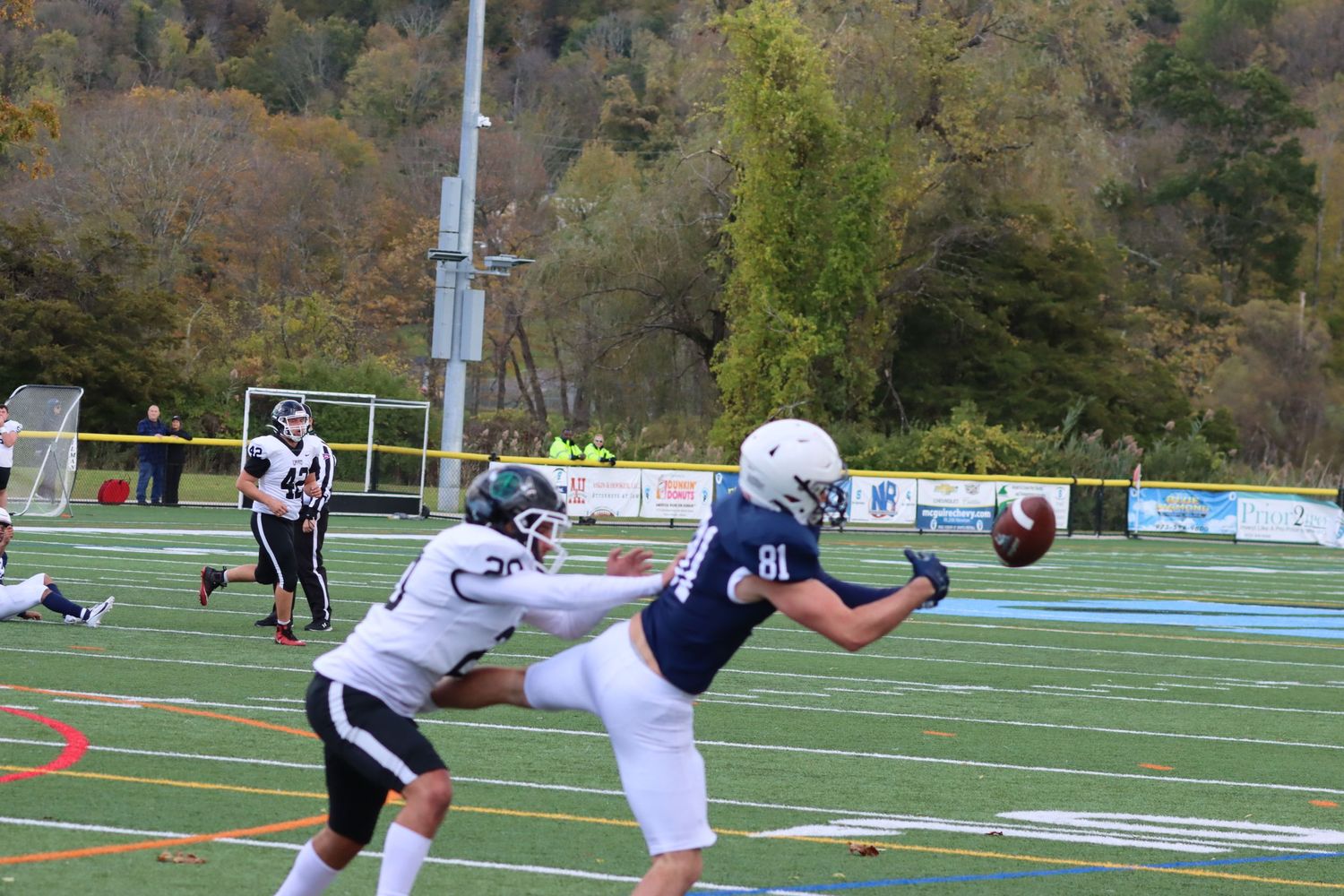 Football player in blue uniform attempts to catch a pass during an autumn college football game.