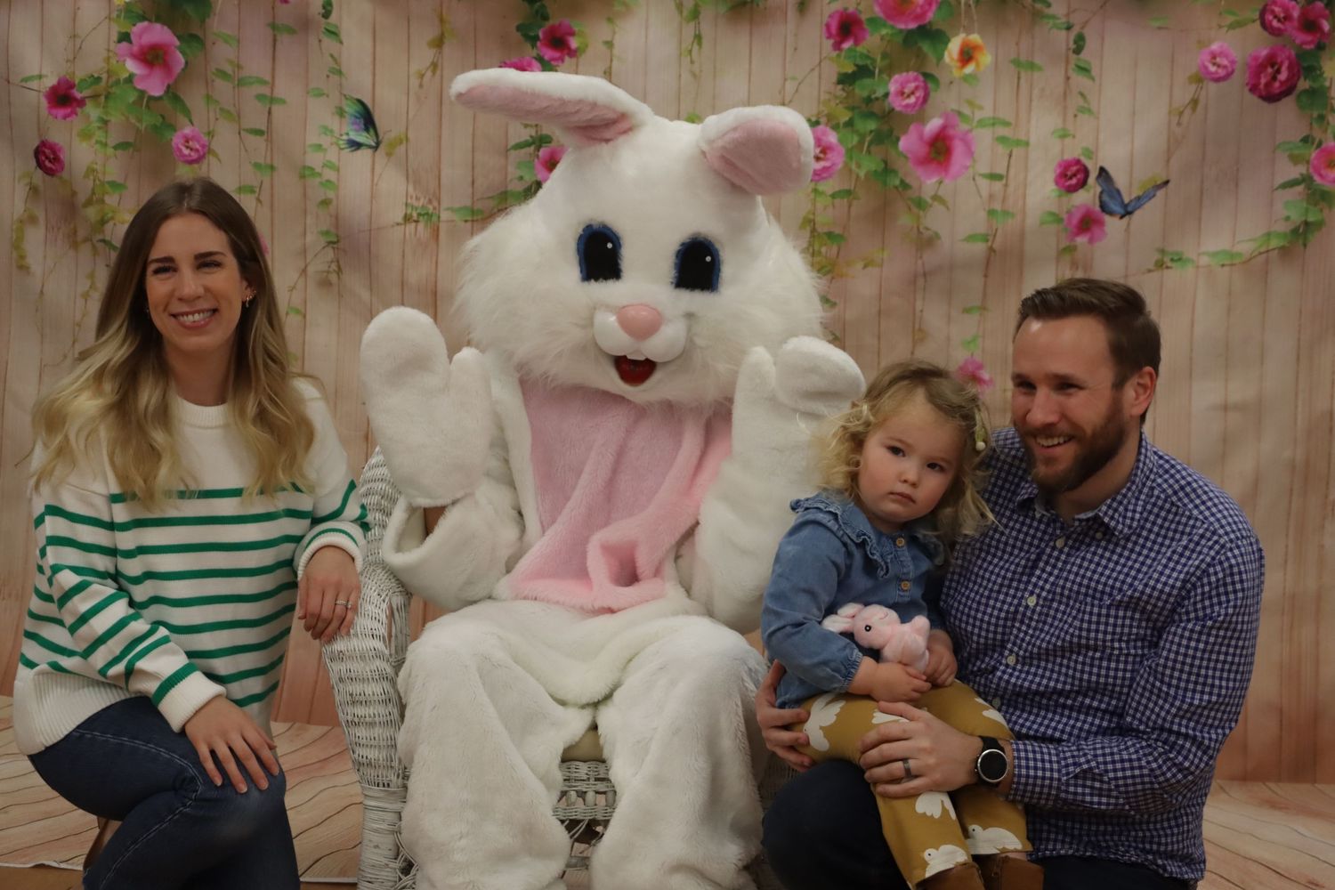 Family with toddler posing with Easter Bunny character in front of floral spring backdrop.
