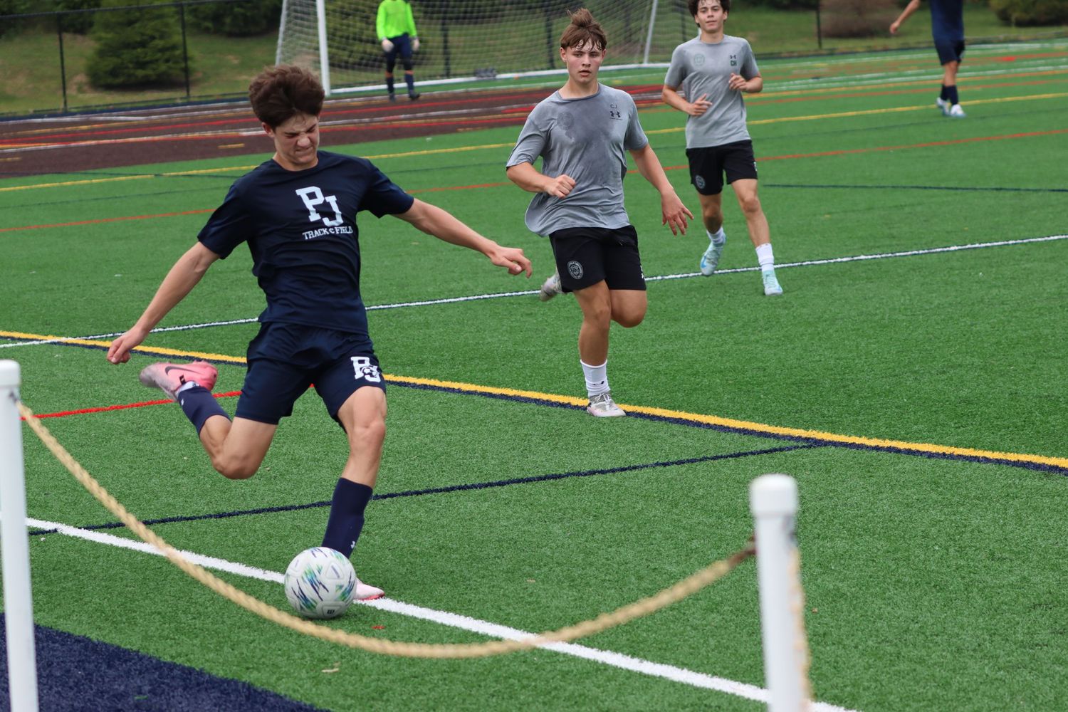 Teen boy kicking a soccer ball on a turf field during a competitive youth soccer match.