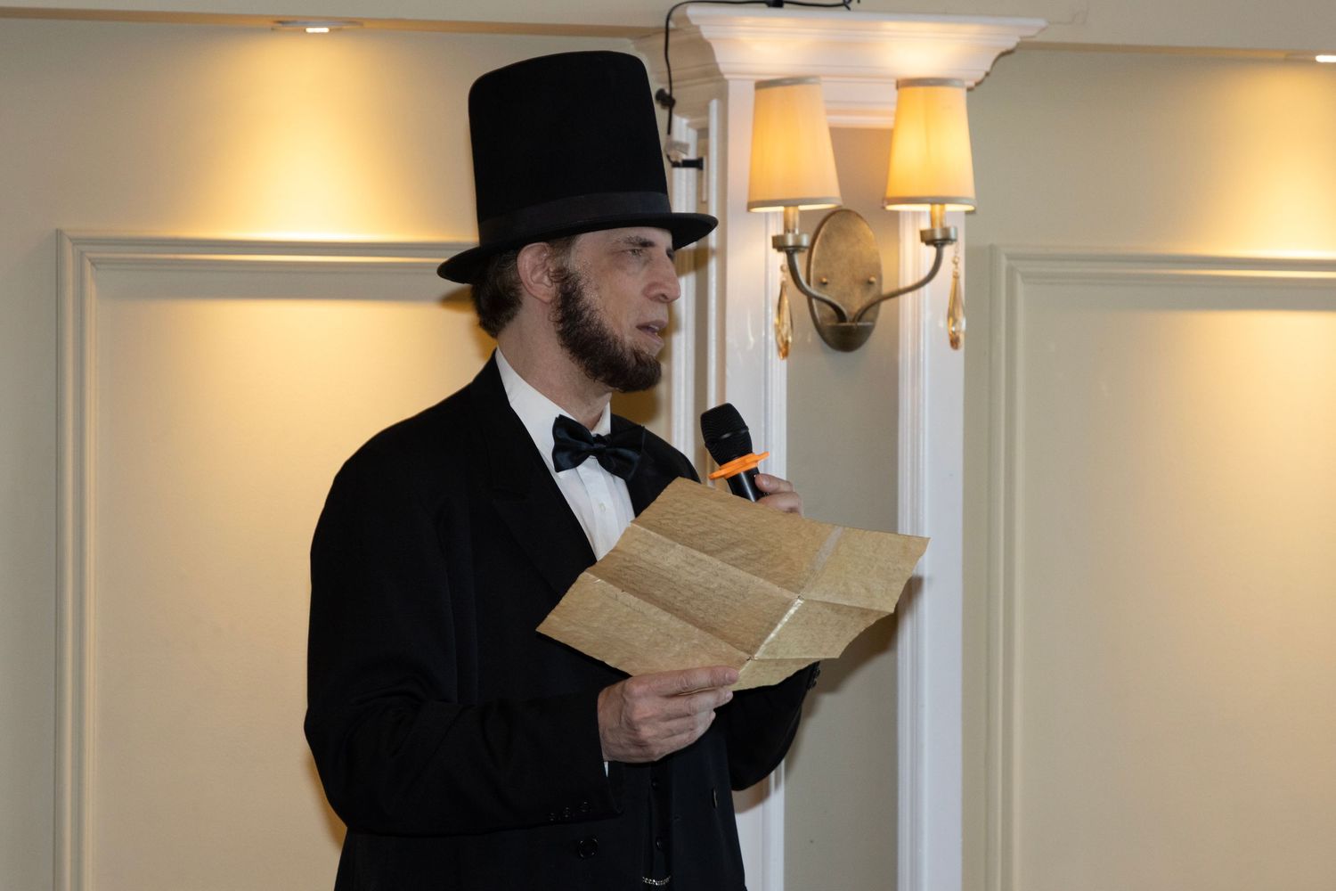 An Abraham Lincoln impersonator reads from papers while wearing a top hat.