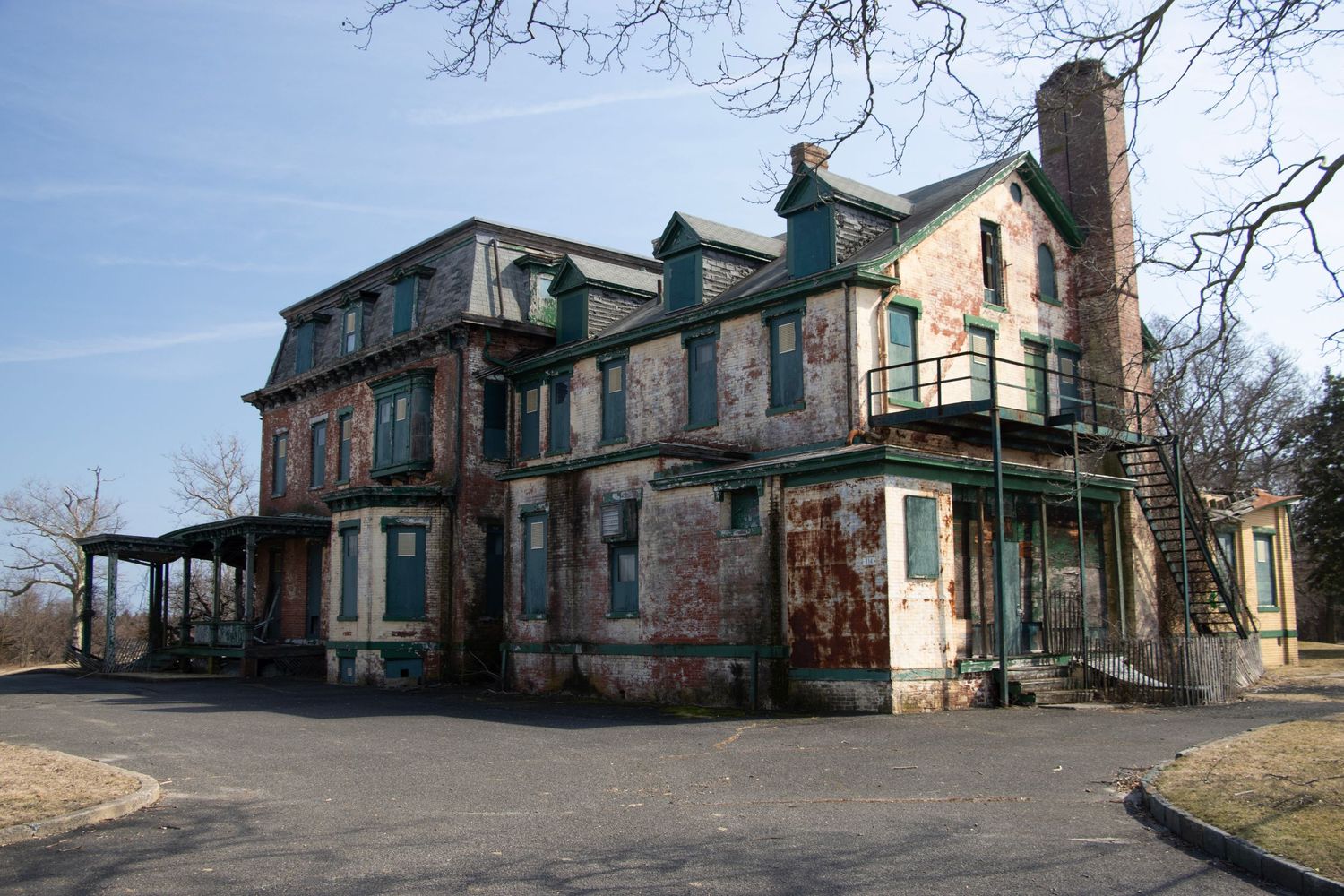 An abandoned Victorian-era brick mansion with deteriorating facade stands against a clear winter sky.