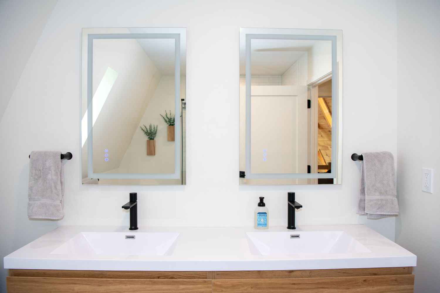Modern white bathroom vanity with black faucet and rectangular mirrors against white wall.