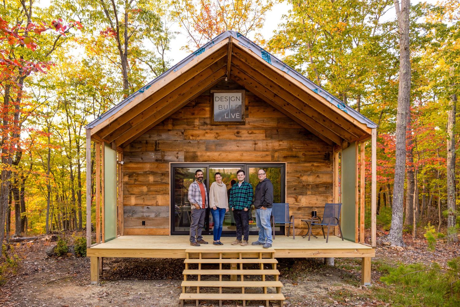 Panoramic view of rustic wooden cabin exterior with autumn foliage and covered porch.
