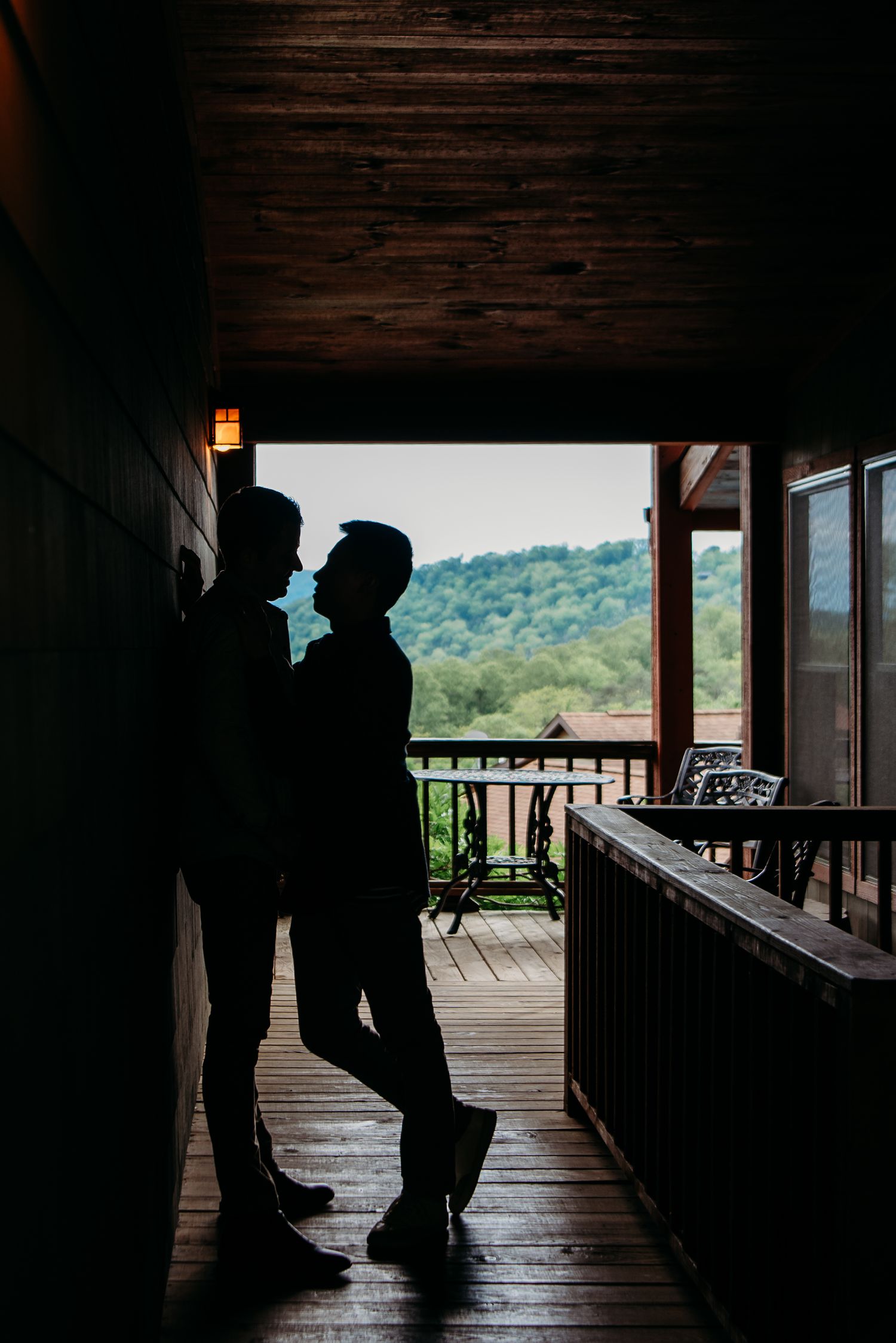 Silhouette of a couple standing on a covered wooden porch overlooking green mountains in the background.