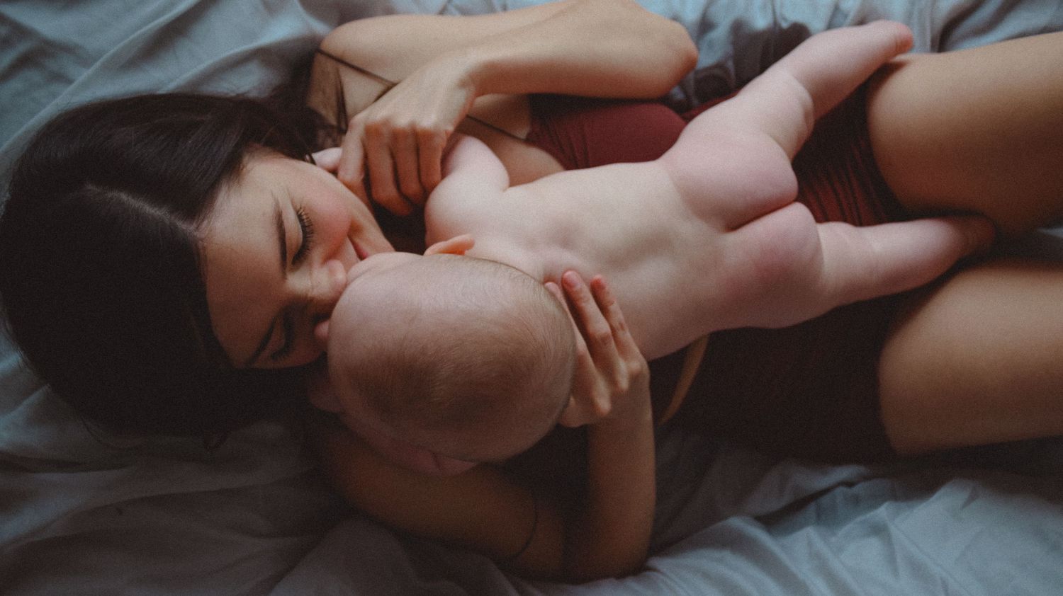A mother and her baby doing skin to skin photographed from above as they are lying on a couch.