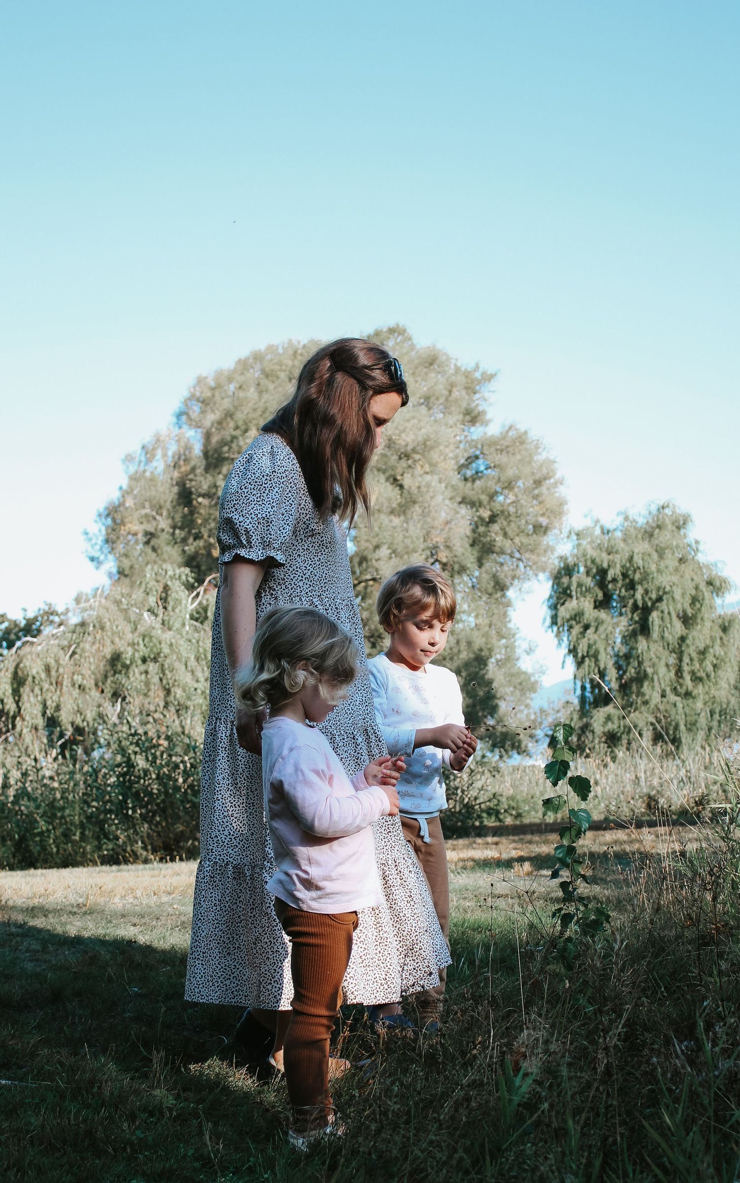 a mother and her two children picking flowers below a beautiful blue sky.